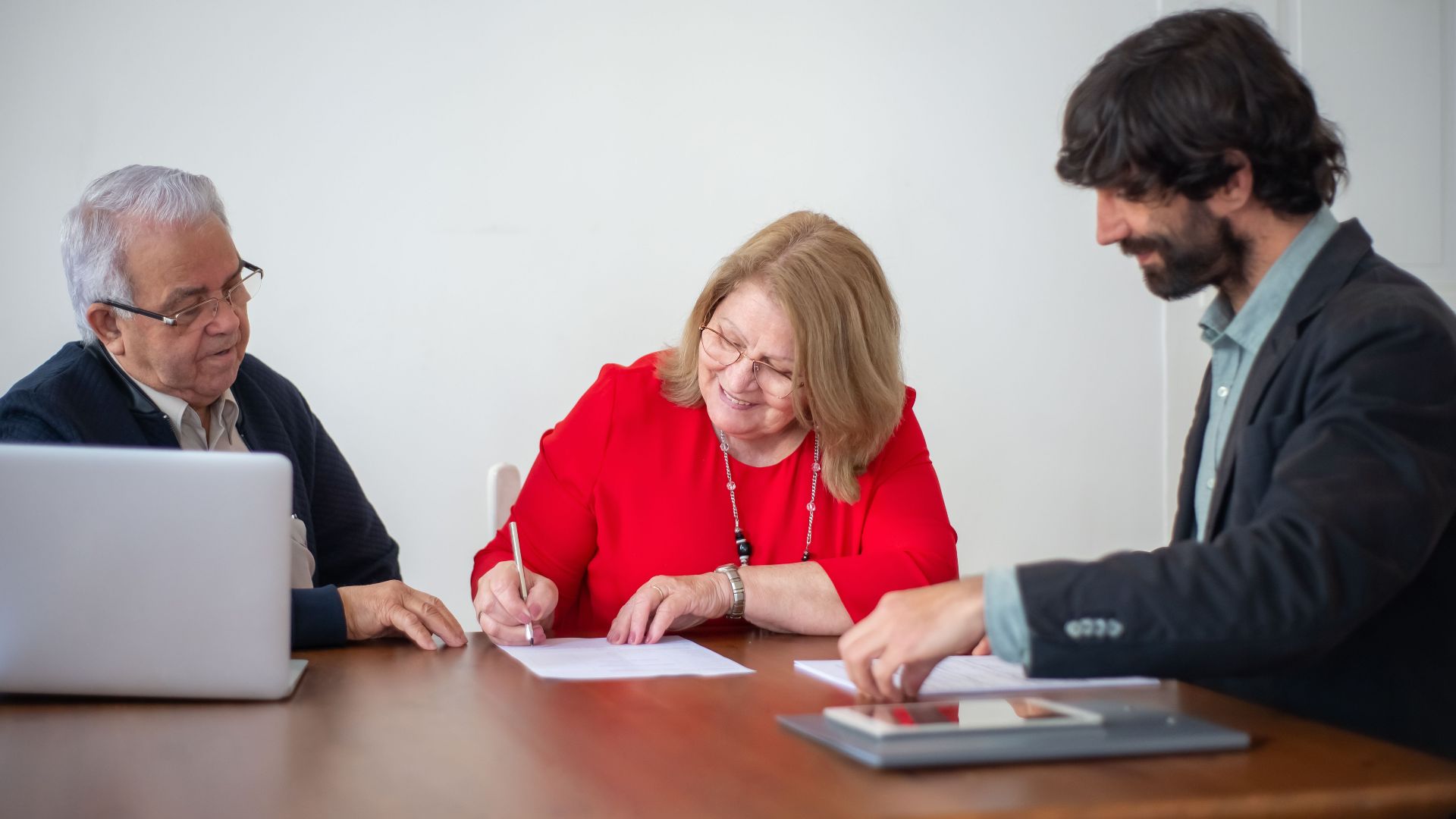 Senior business professionals signing documents during a meeting in a bright office.