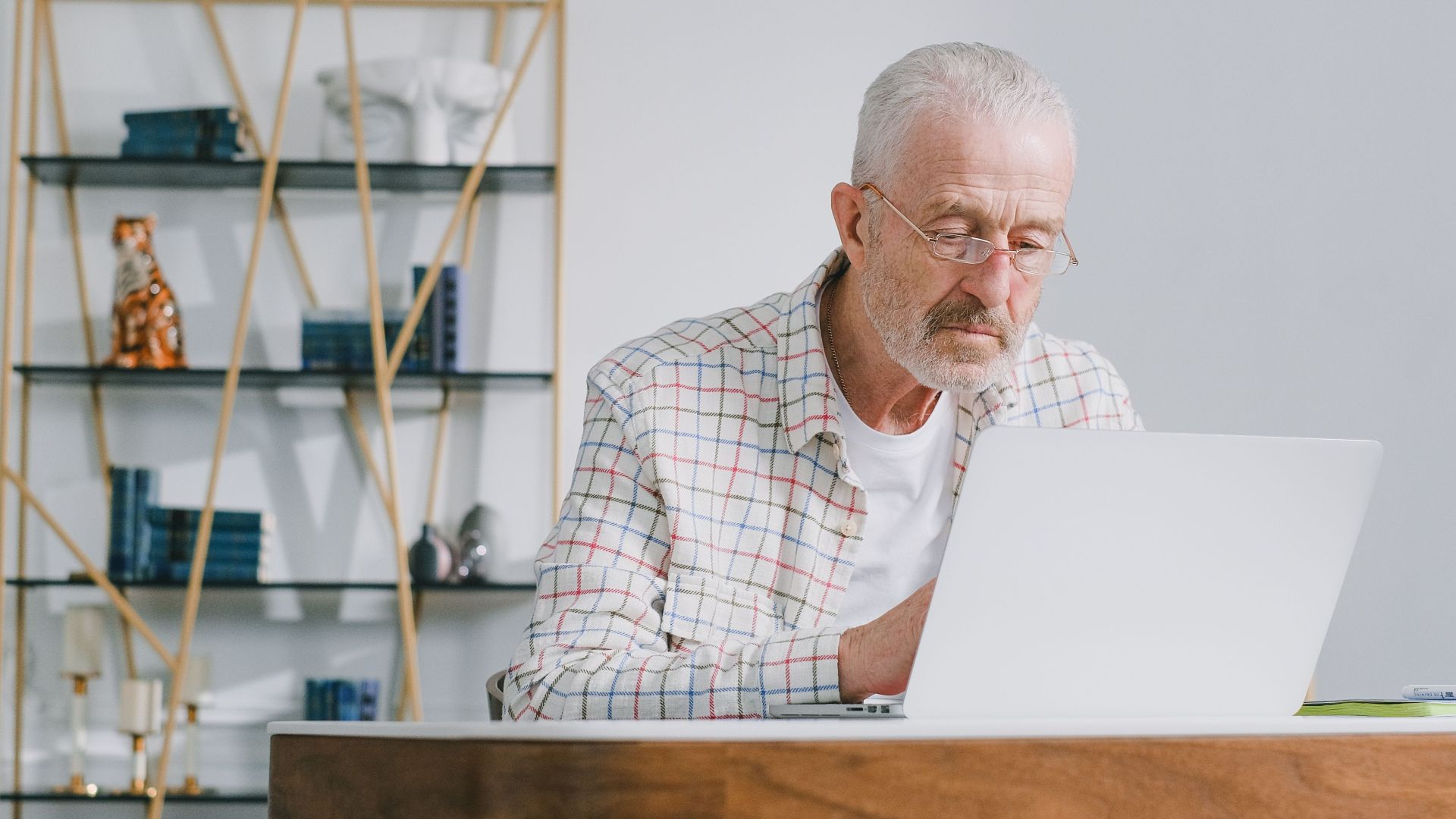 Elderly man using a laptop at home, focused on modern technology in a bright room.