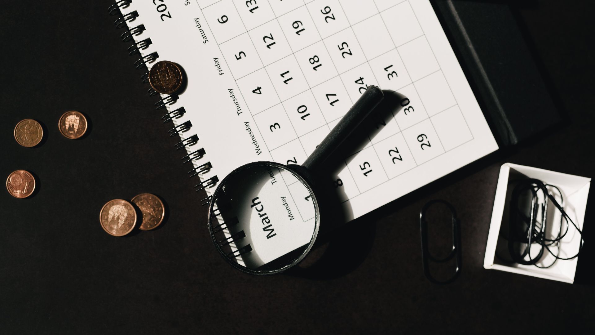 Top view of a calendar with a magnifying glass and coins, ideal for financial themes.