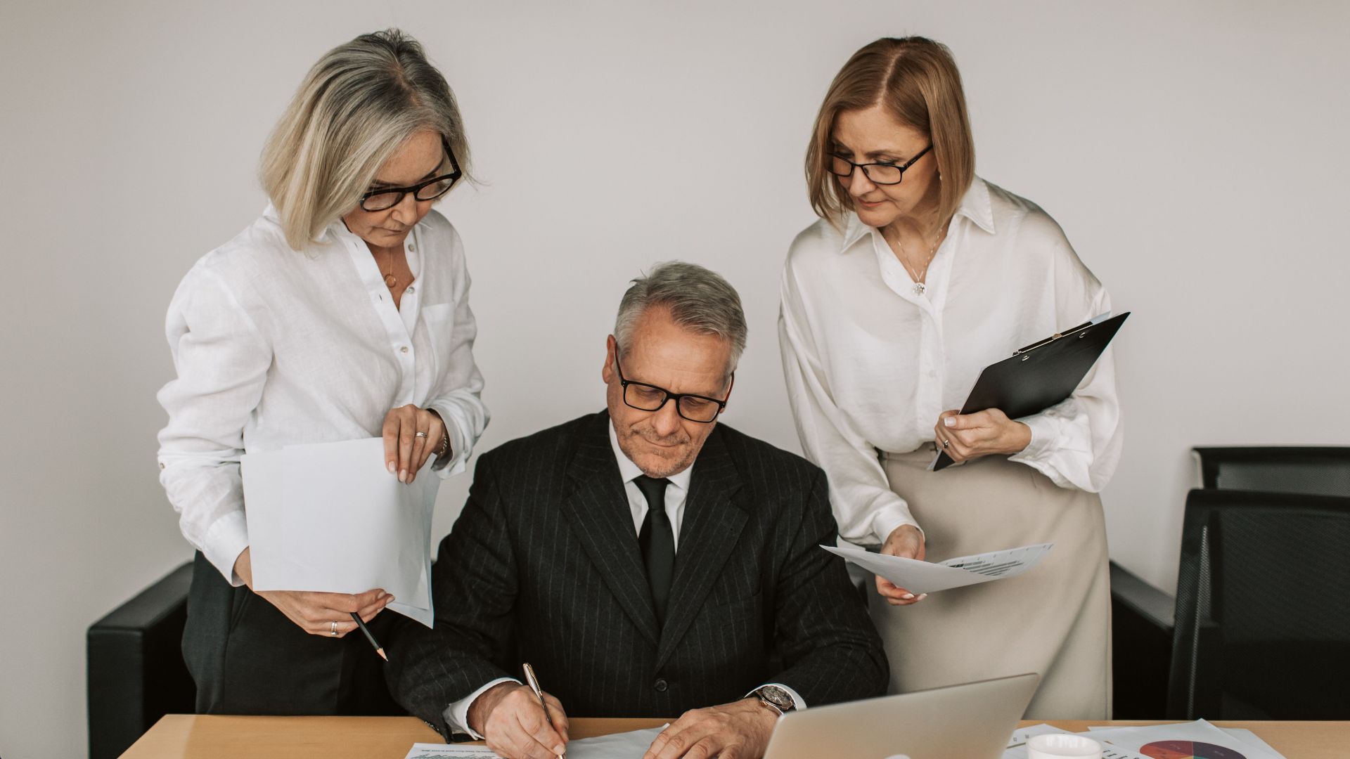 Three mature professionals collaborate at an office desk, analyzing charts and documents.