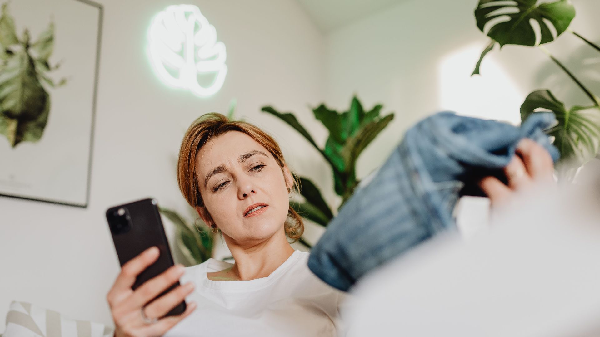 Woman browsing online fashion while relaxing amidst indoor plants.