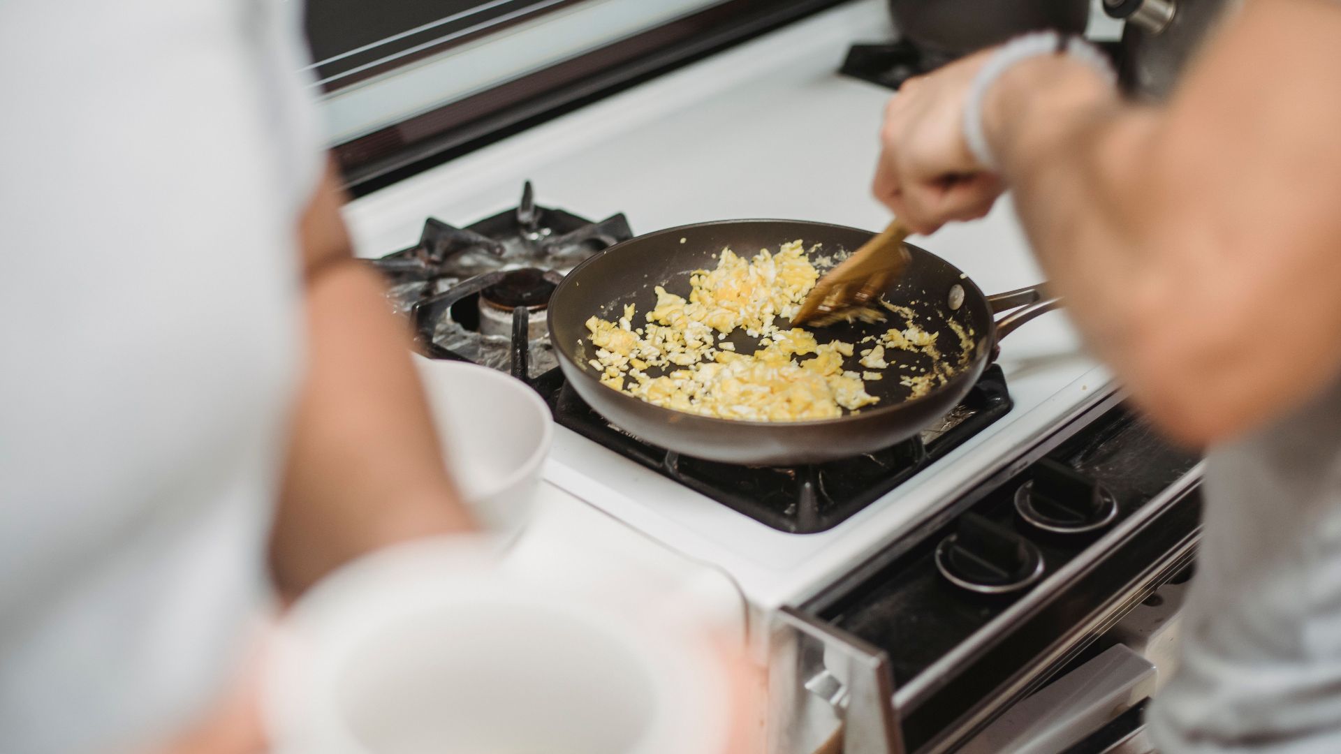Close-up of a person cooking scrambled eggs on a stovetop, highlighting a cozy kitchen setting.