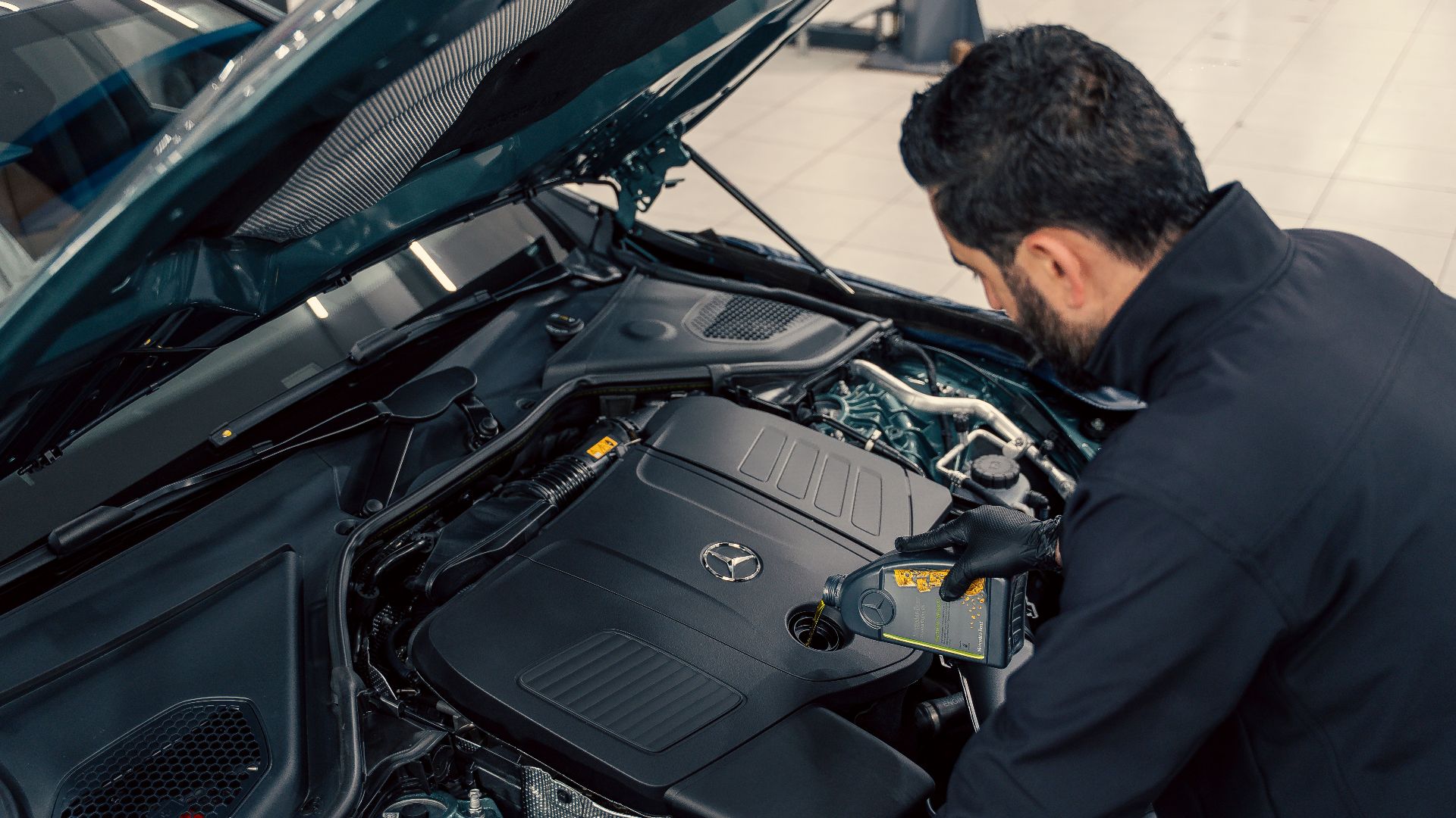 Mechanic inspecting and filling engine oil in a car at an indoor service center.