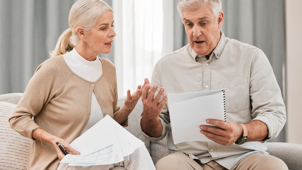 Shutterstock-2368562285, Stress, old couple with documents and taxes in home, mortgage payment and retirement funding crisis. Financial budget, senior man and woman on sofa with anxiety for bills, life insurance and debt.