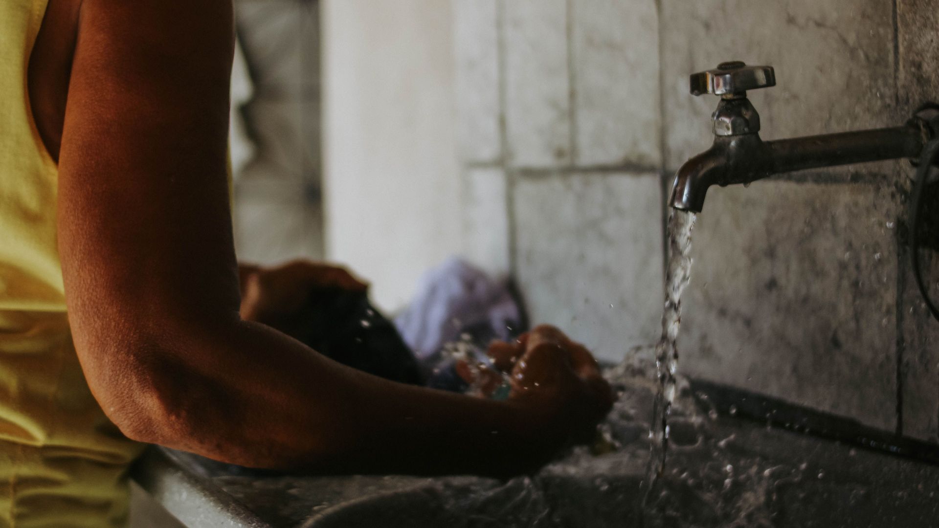 Close-up of a person washing clothes in a sink with running water indoors.