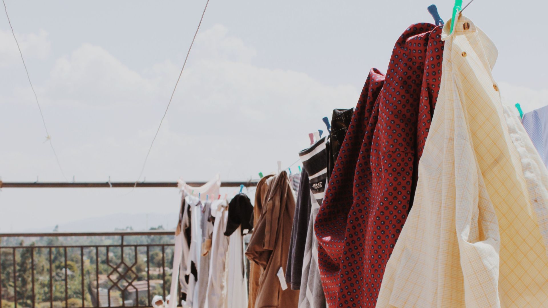 Colorful laundry hanging on a balcony clothesline under a sunny sky.