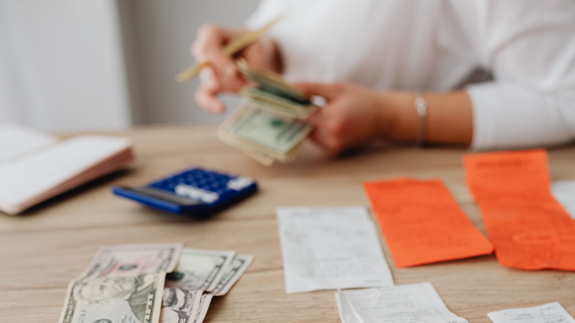 A person using a calculator and cash to plan a household budget.