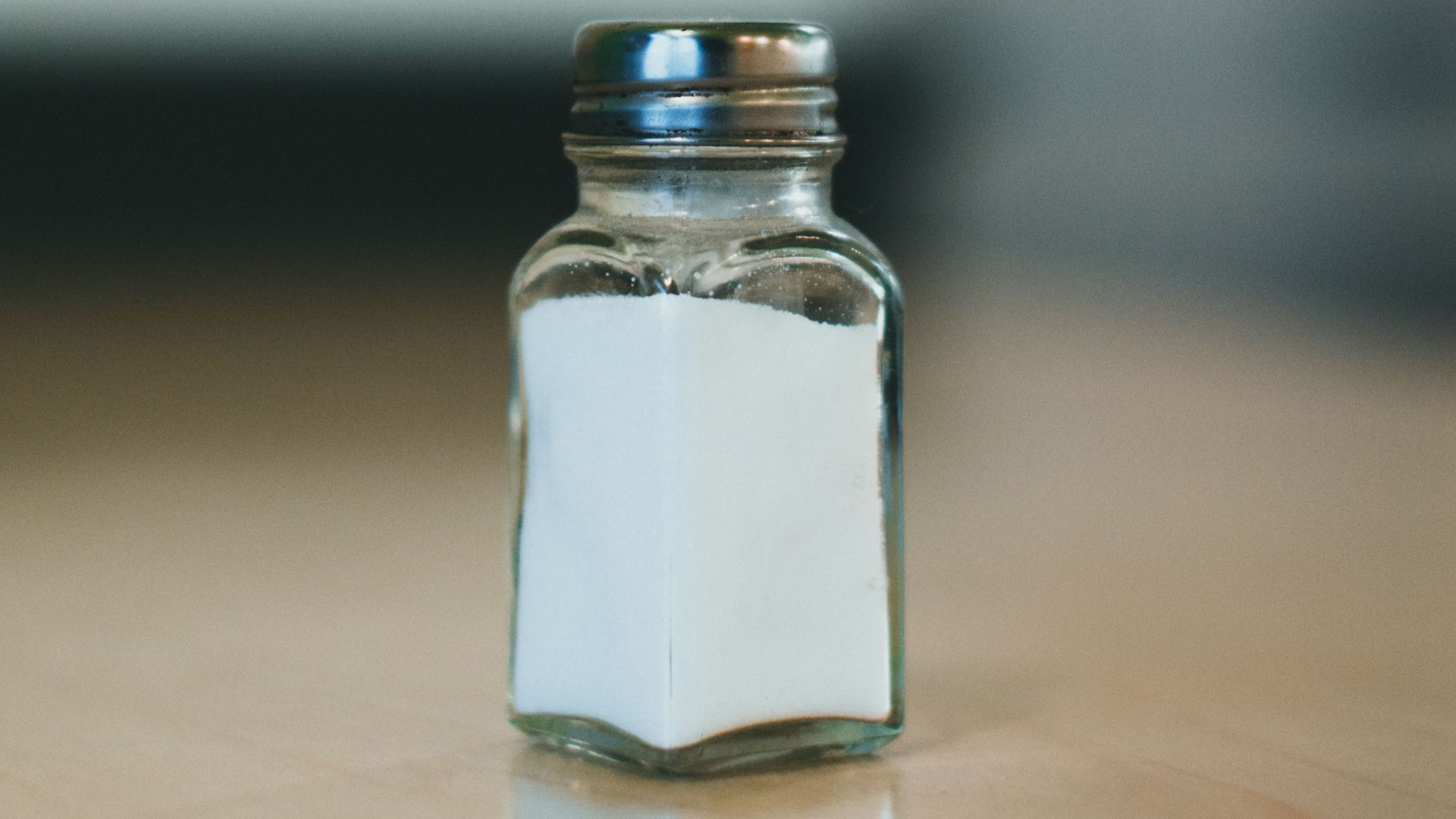 Close-up of a salt shaker on a wooden surface with blurred background, offering ample copyspace.