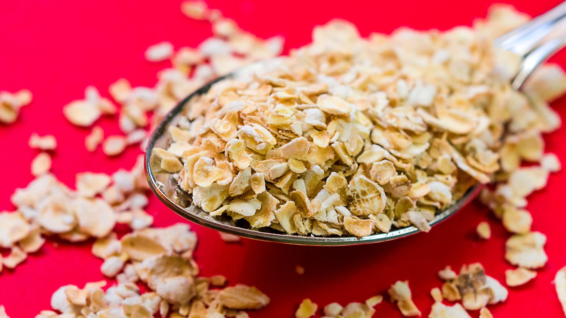 Close-up image of oats scattered on a spoon with vivid red background, perfect for food advertising.