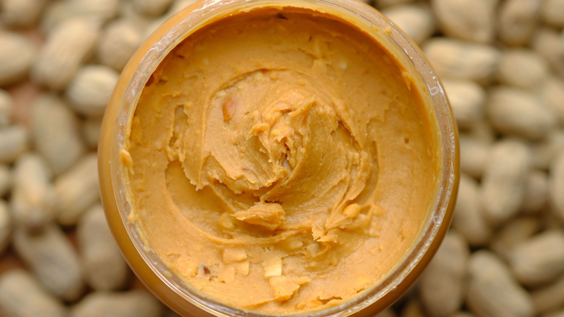 Close-up of creamy peanut butter in a glass jar surrounded by peanuts. Tasty and homemade.