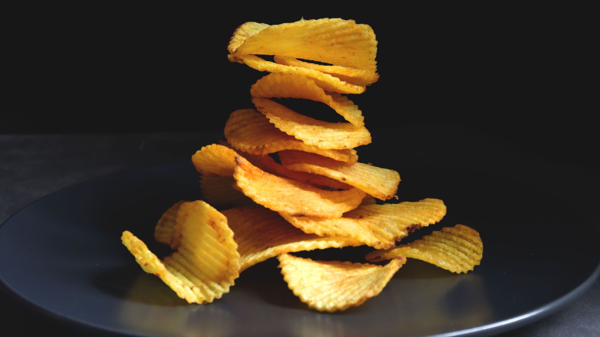 A delicious stack of golden ripple potato chips placed on a sleek black plate.