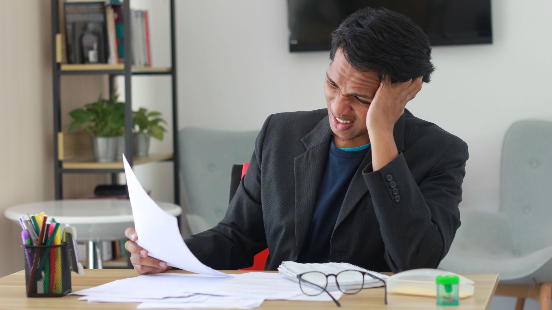 A businessman in an office experiencing stress while reviewing documents.