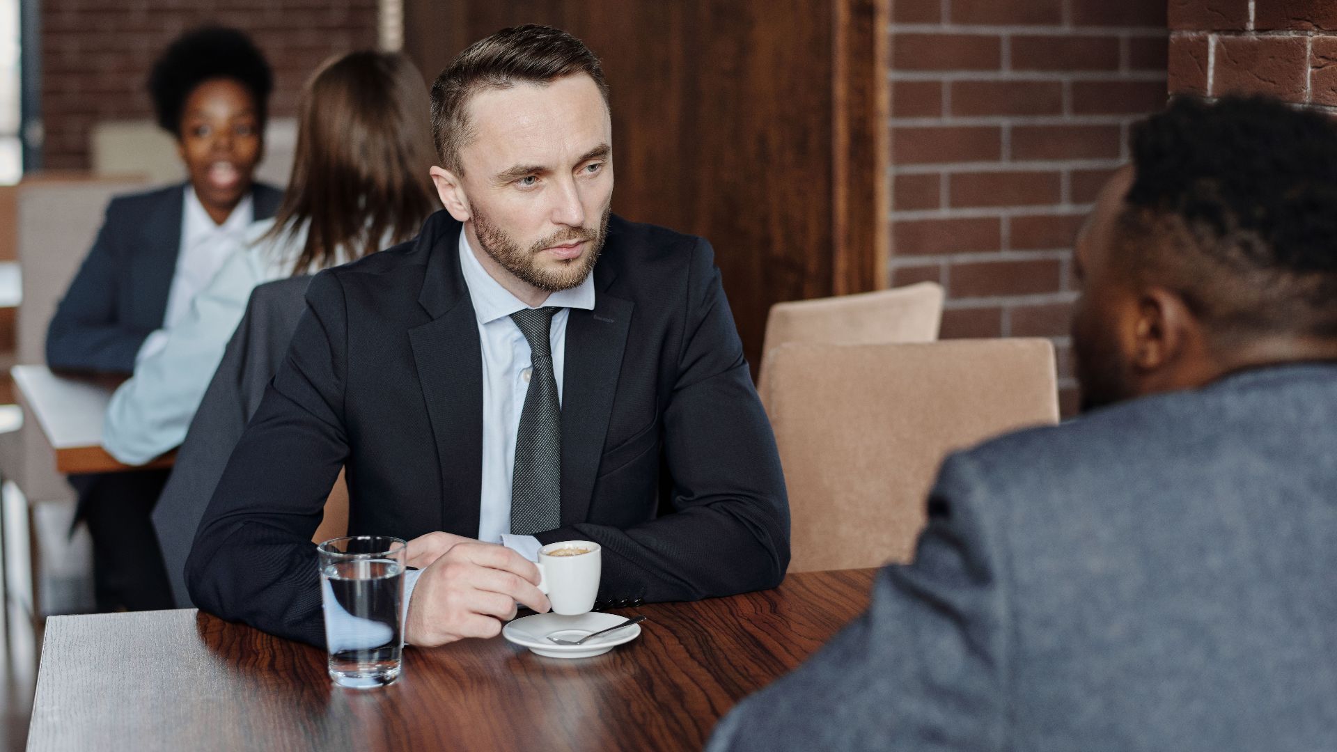 Two businessmen in suits discussing over coffee during a meeting in a café.