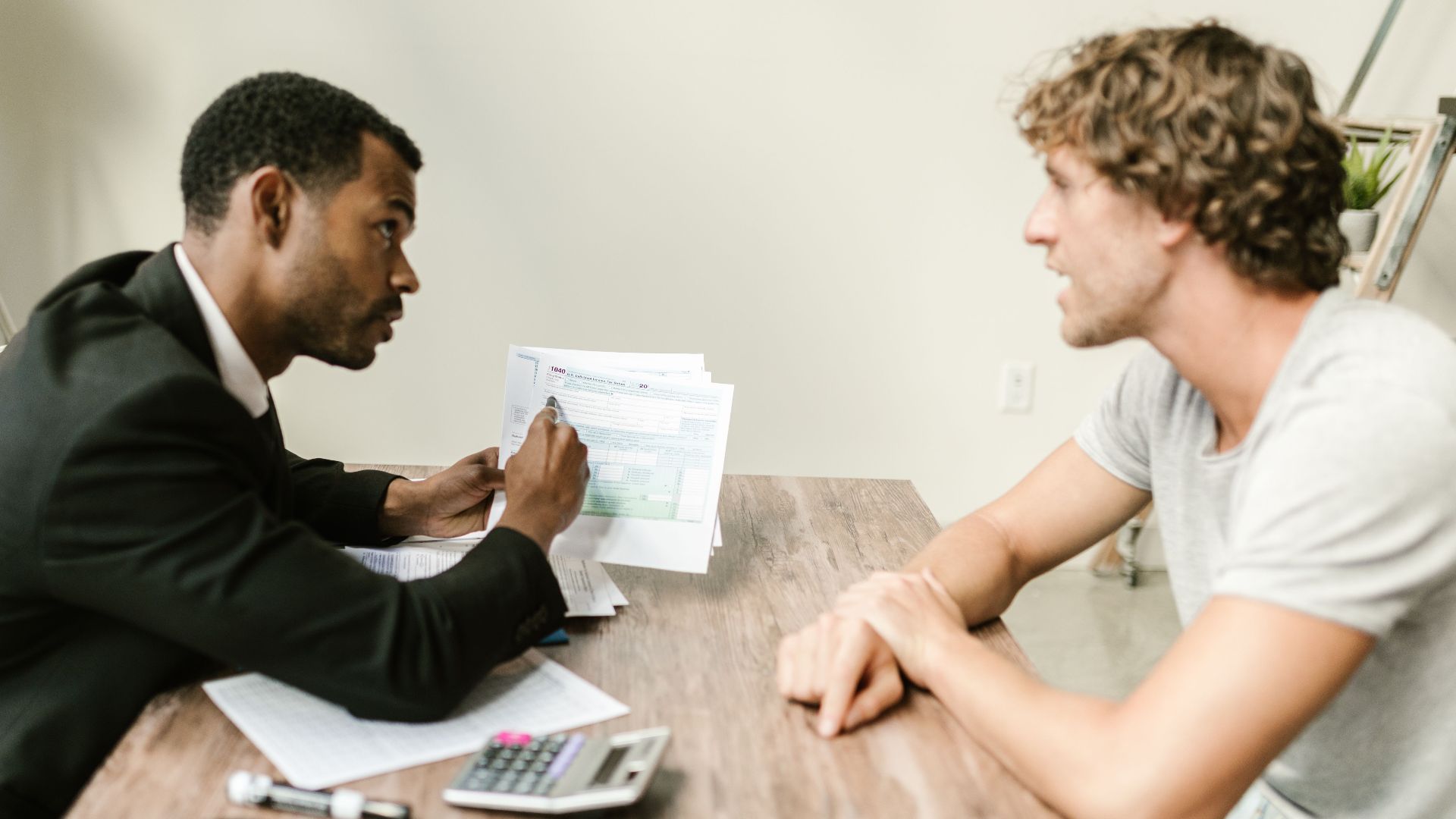 A financial advisor discusses paperwork with a client at a desk in a modern office.