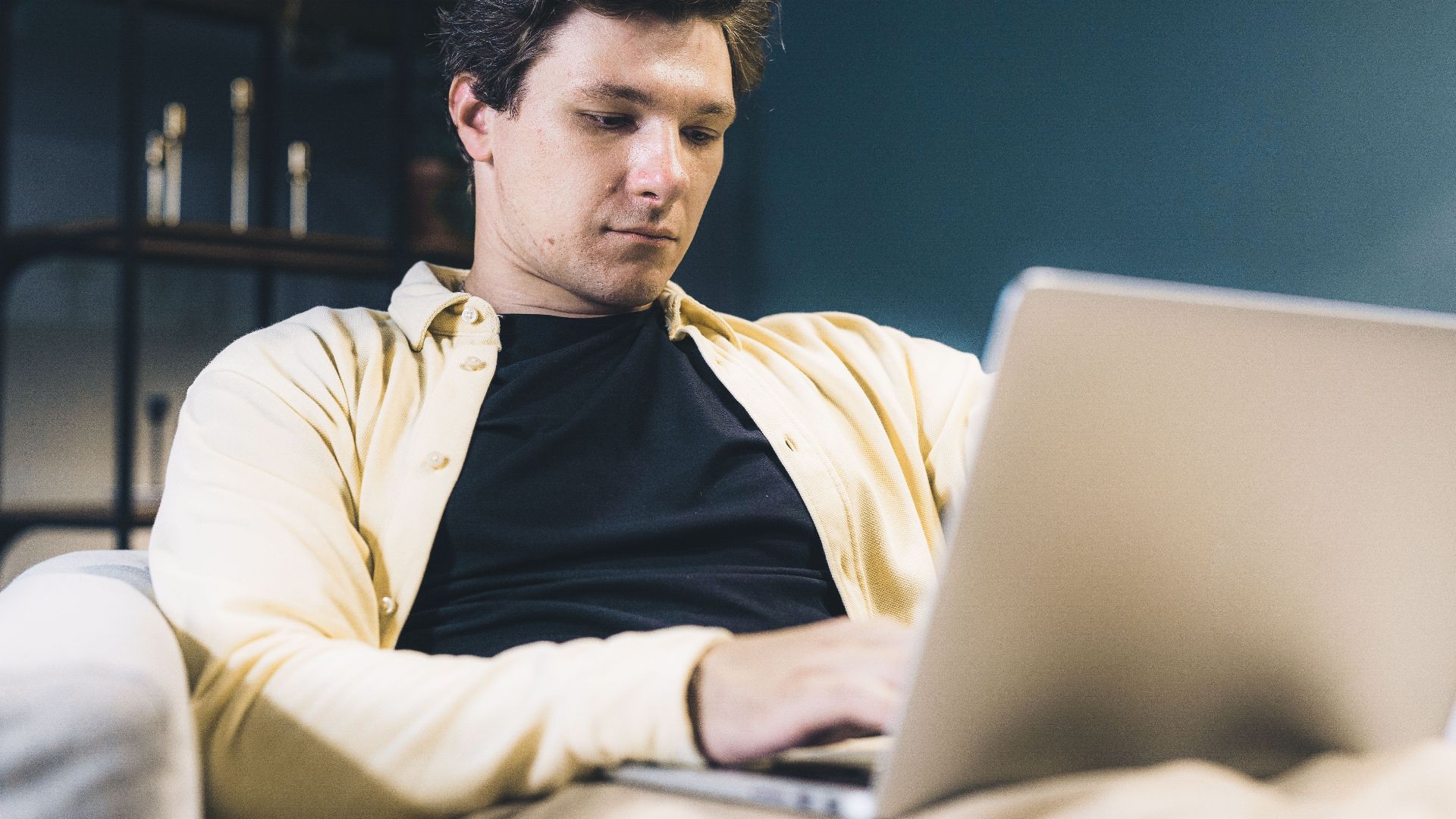 Focused young man sitting comfortably using a laptop at home, engaging in remote work.