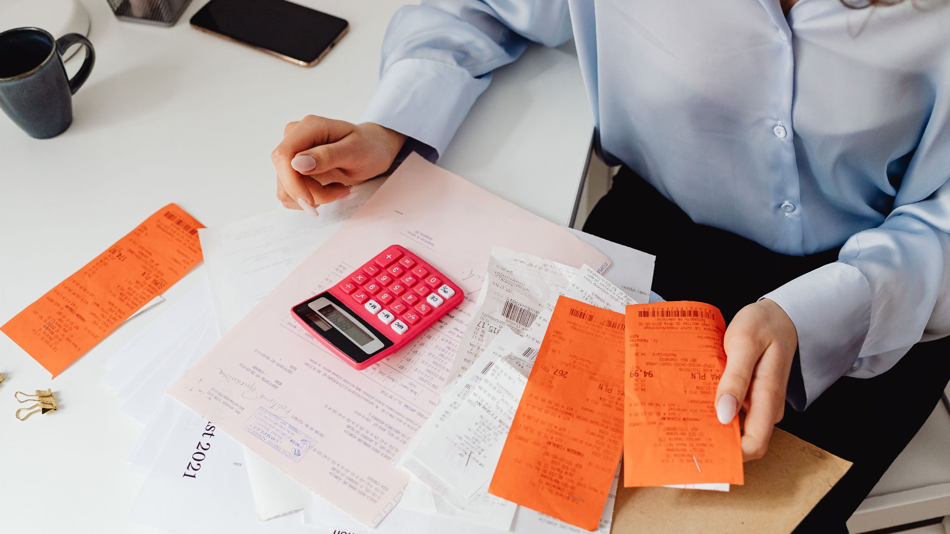 A woman reviews receipts and calculates expenses at a desk with a pink calculator.