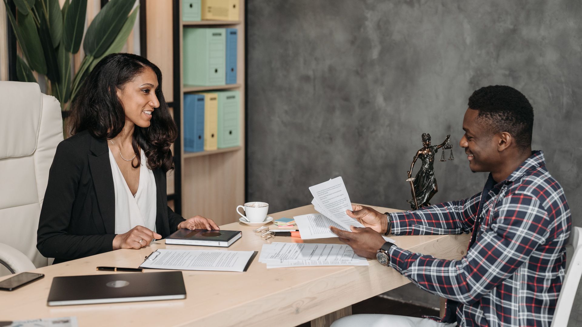 Two professionals having a discussion in a stylish office with paperwork and a laptop.