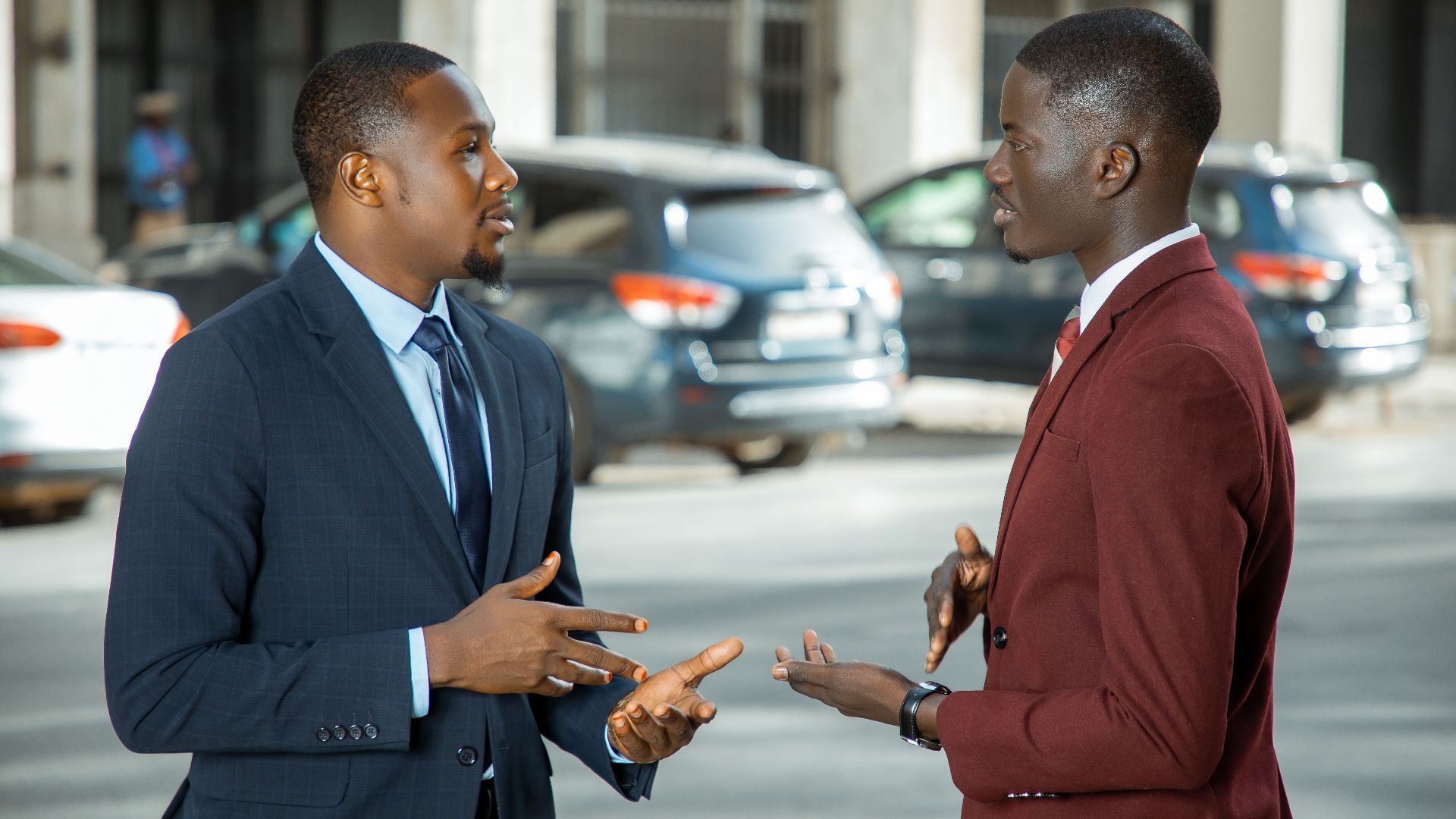 Two African businessmen in formal suits have a discussion on a city street in Dakar, Senegal.