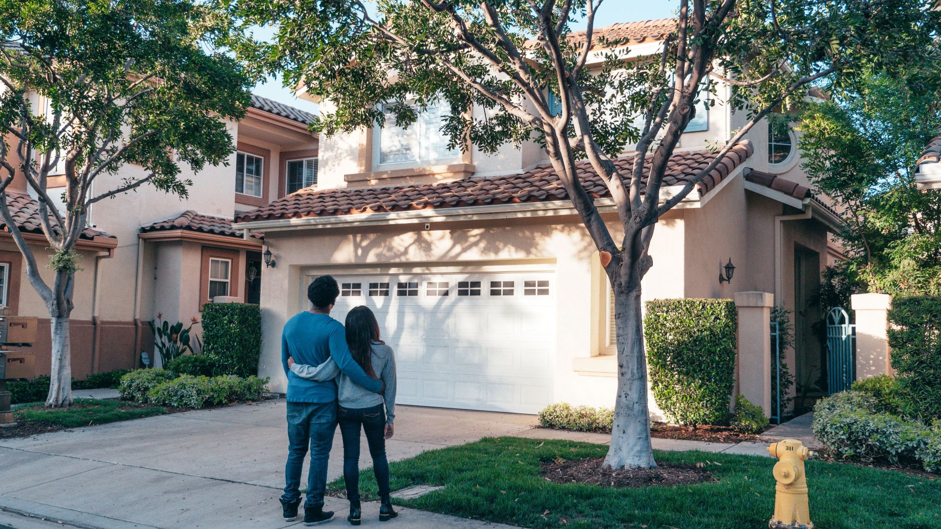 Couple hugging outside their newly purchased suburban home, showcasing togetherness and new beginnings.