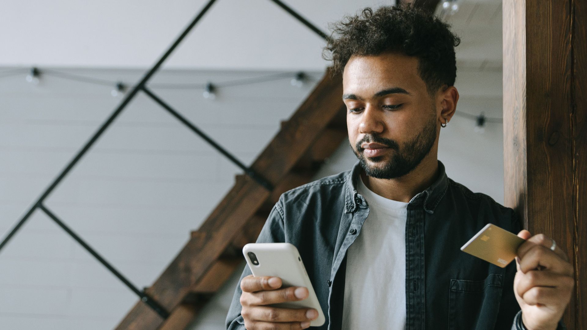 A young man using a smartphone and credit card for online shopping indoors.