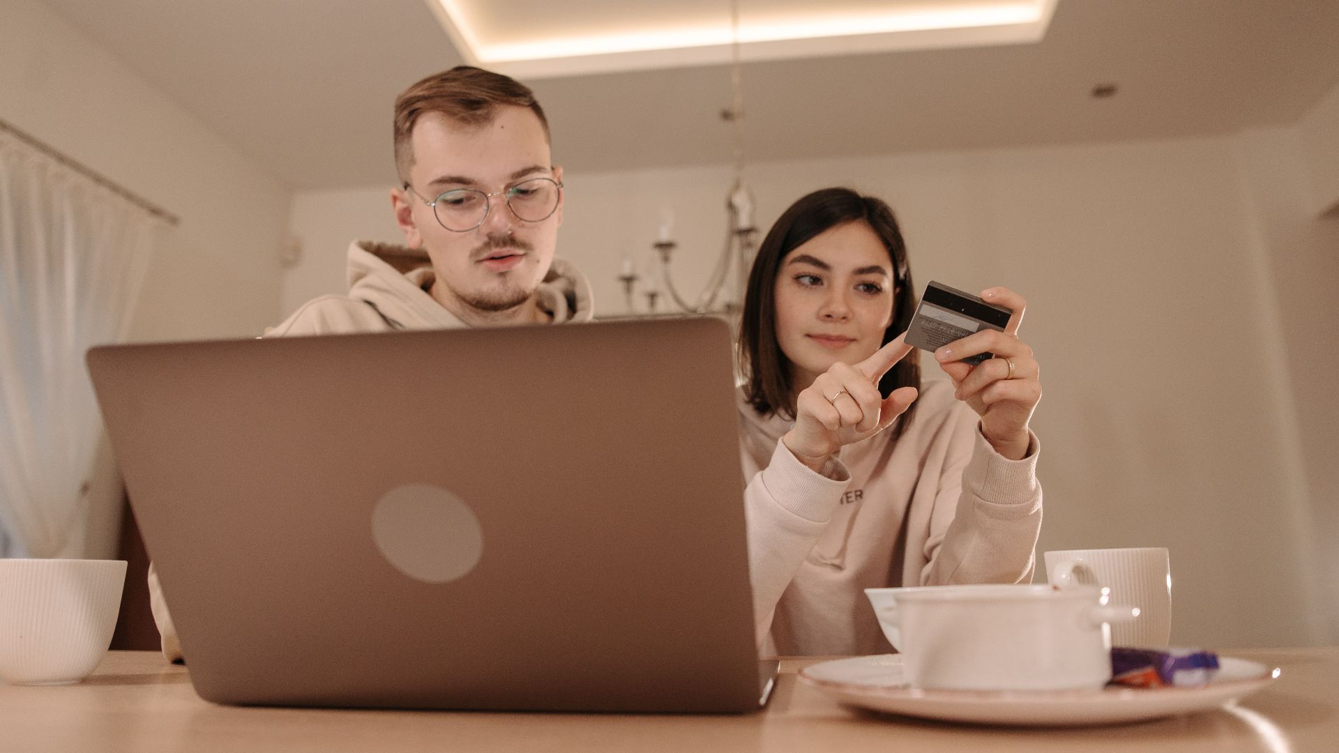 A young couple using a laptop and credit card for online shopping in a cozy indoor setting.