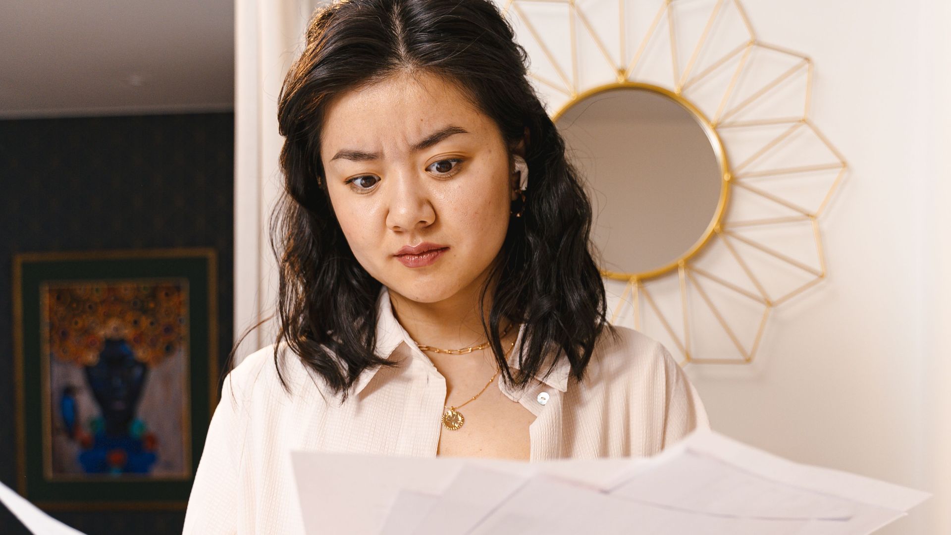 Young woman looks confused while reviewing documents in a modern home interior.