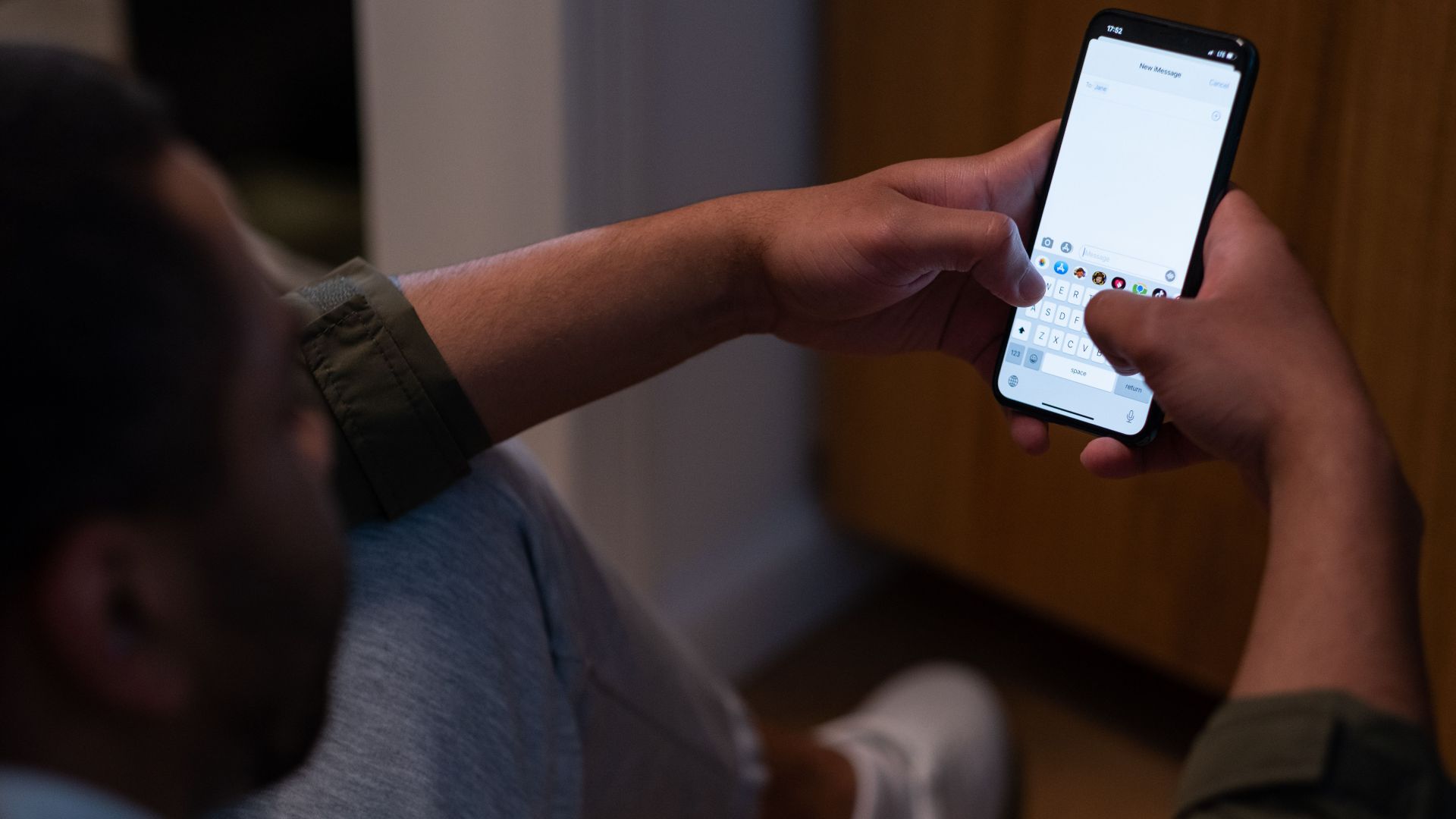 Close-up of a man texting on a smartphone indoors during evening time. Captures modern communication.