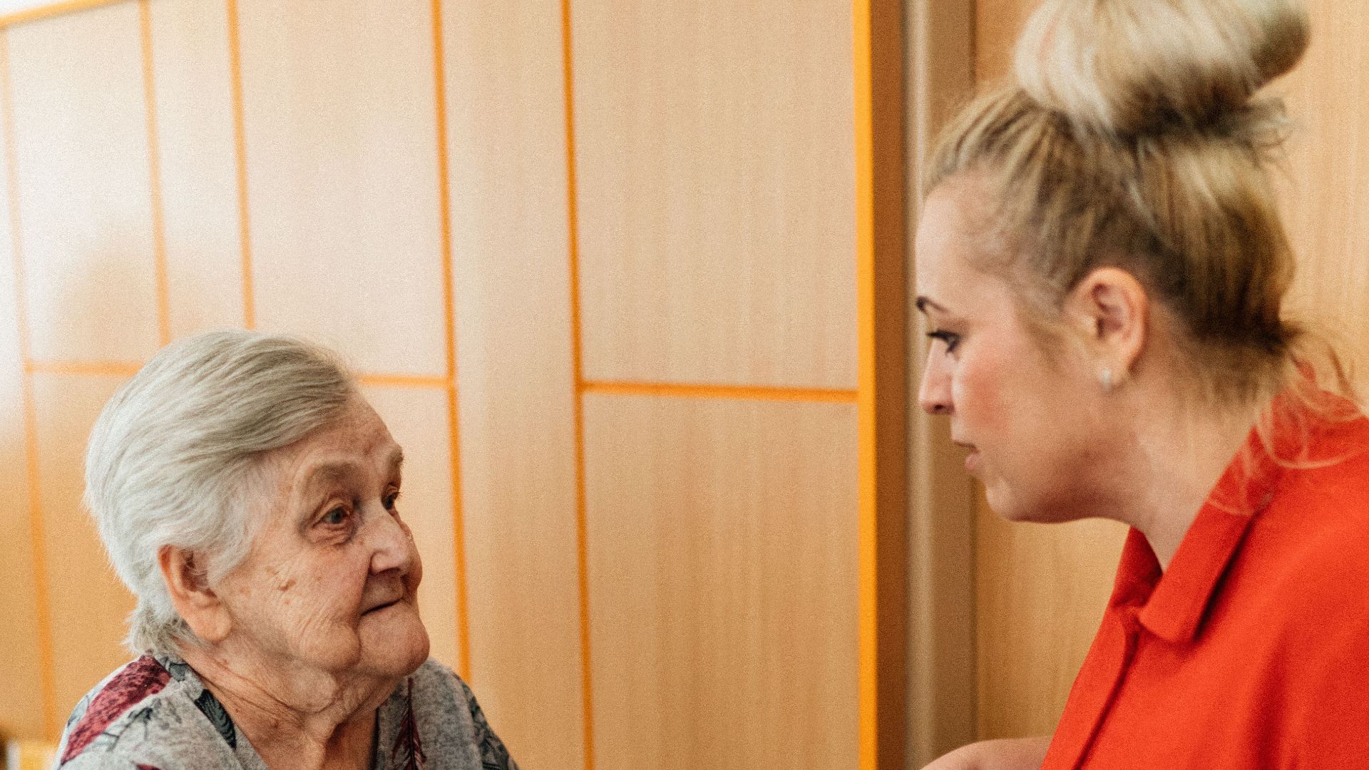 A caregiver assists an elderly woman in a retirement home corridor, fostering companionship and support.