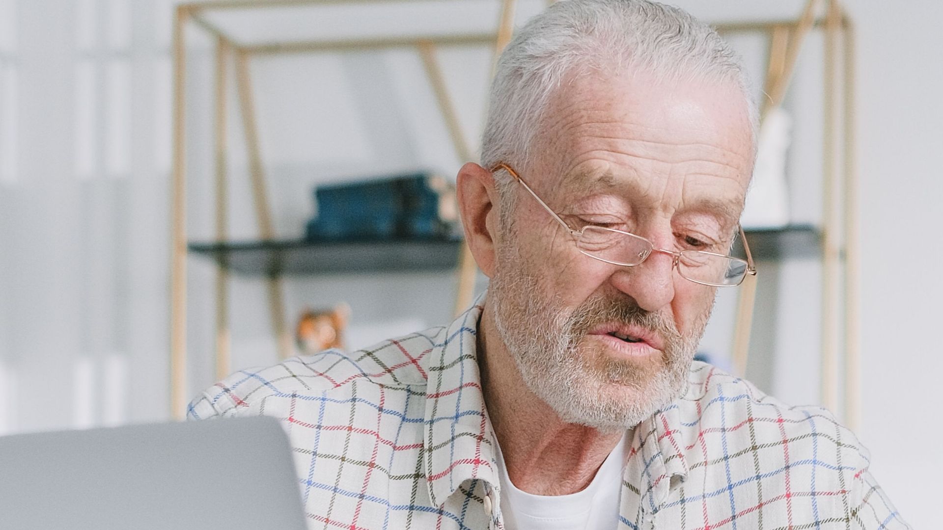 Elderly man reading papers at home with a laptop, emphasizing financial planning.