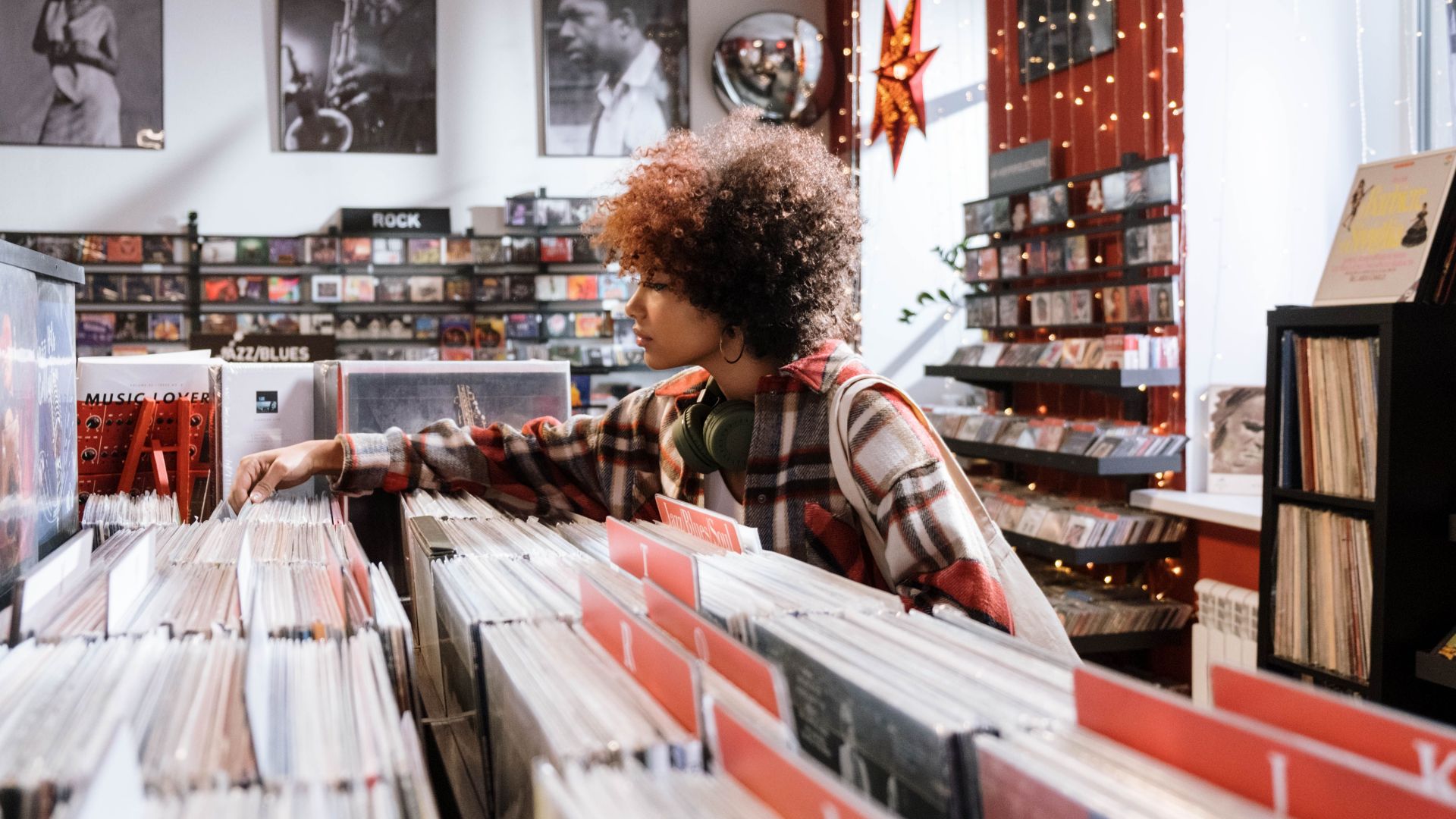Afro-haired woman browsing vintage vinyl records in a cozy music store.