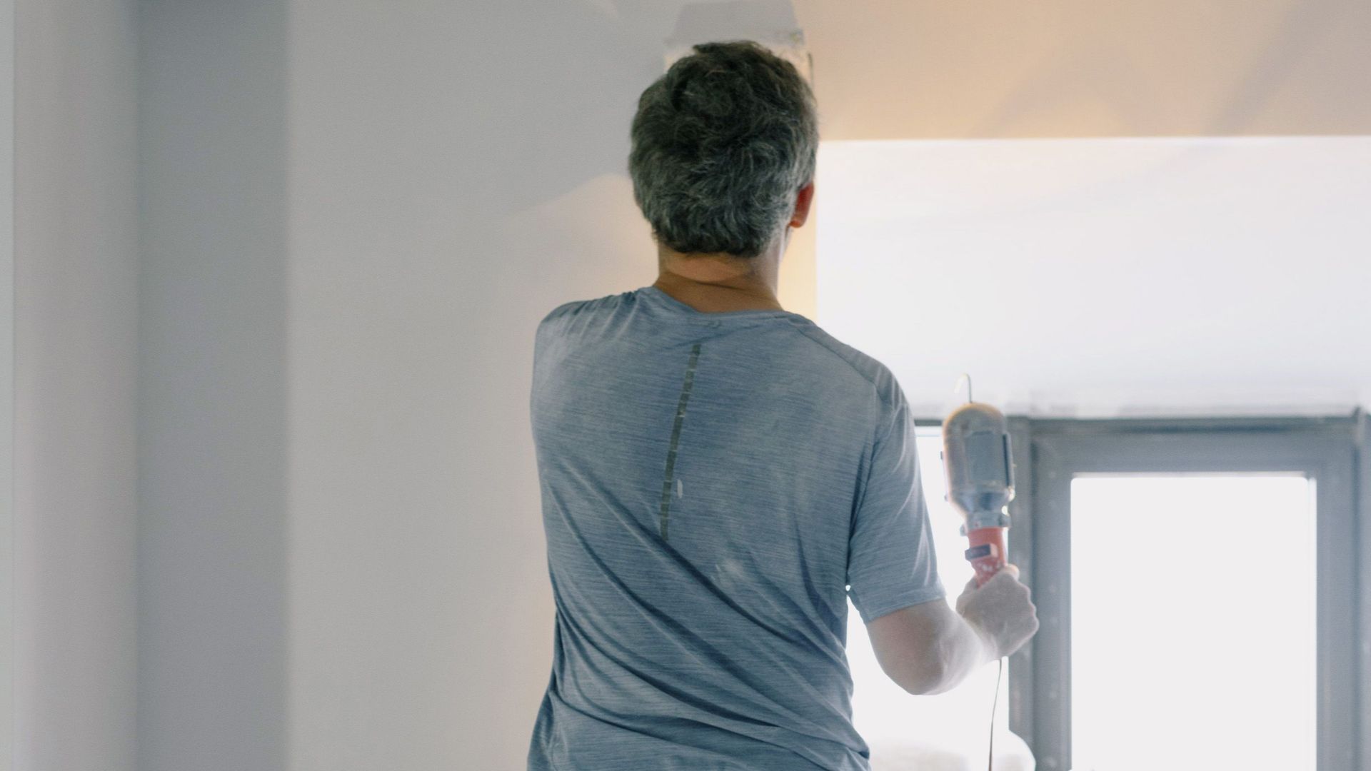 Back view full body of anonymous handyman on ladder doing renovation works in flat