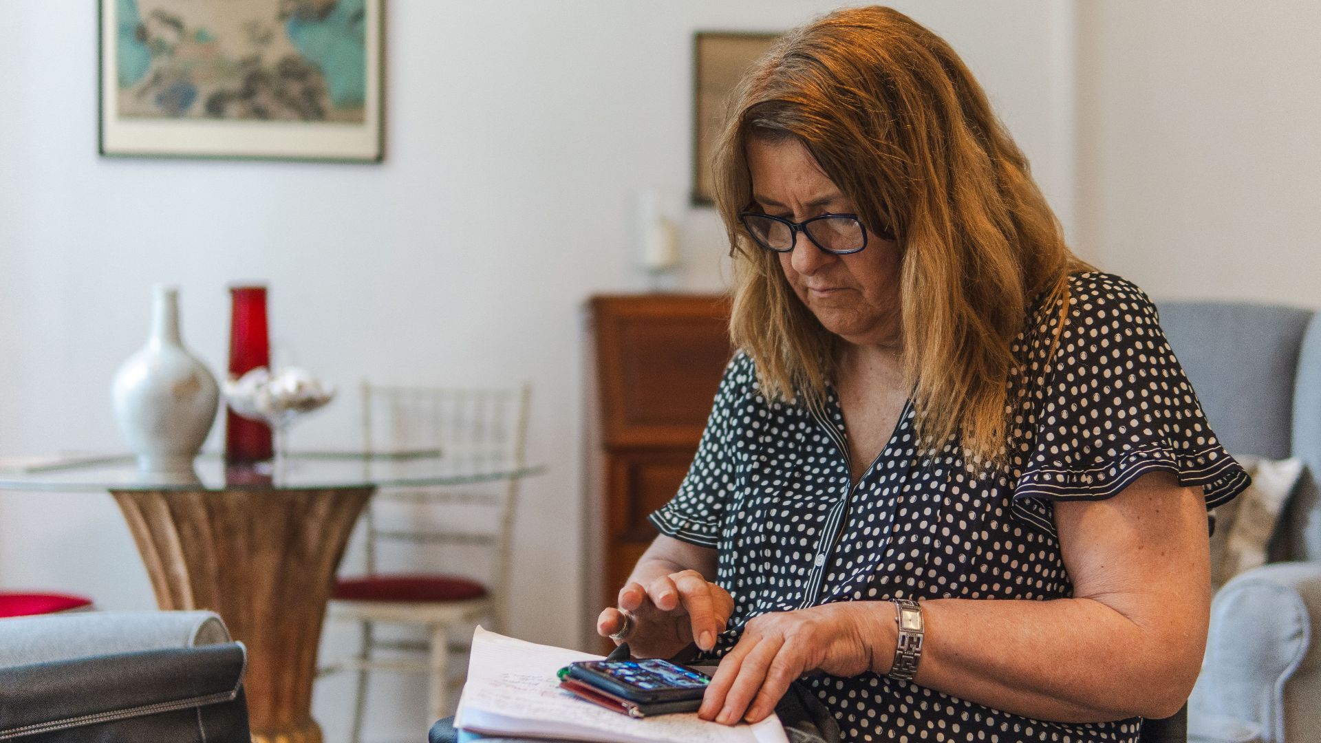 Focused woman calculating expenses with calculator and notebook at home.