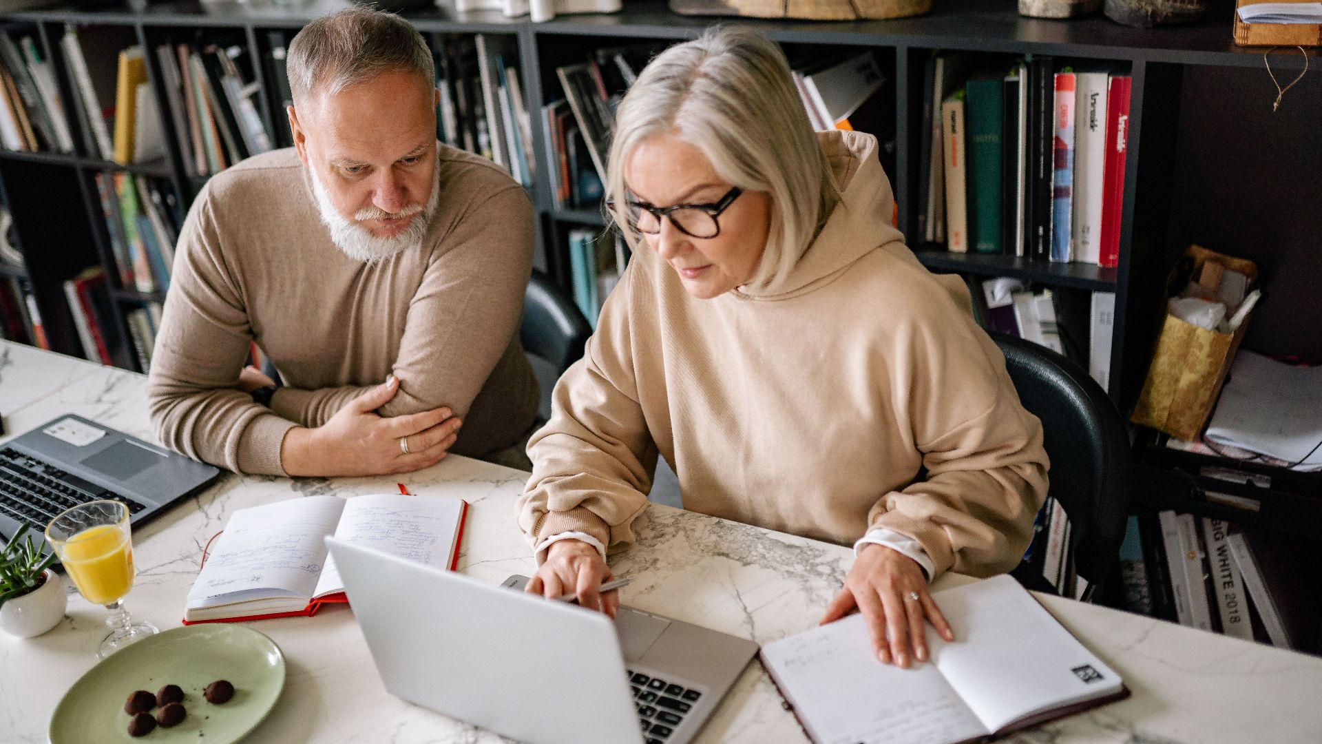 Elderly couple collaborating on laptops in a cozy home office setting.