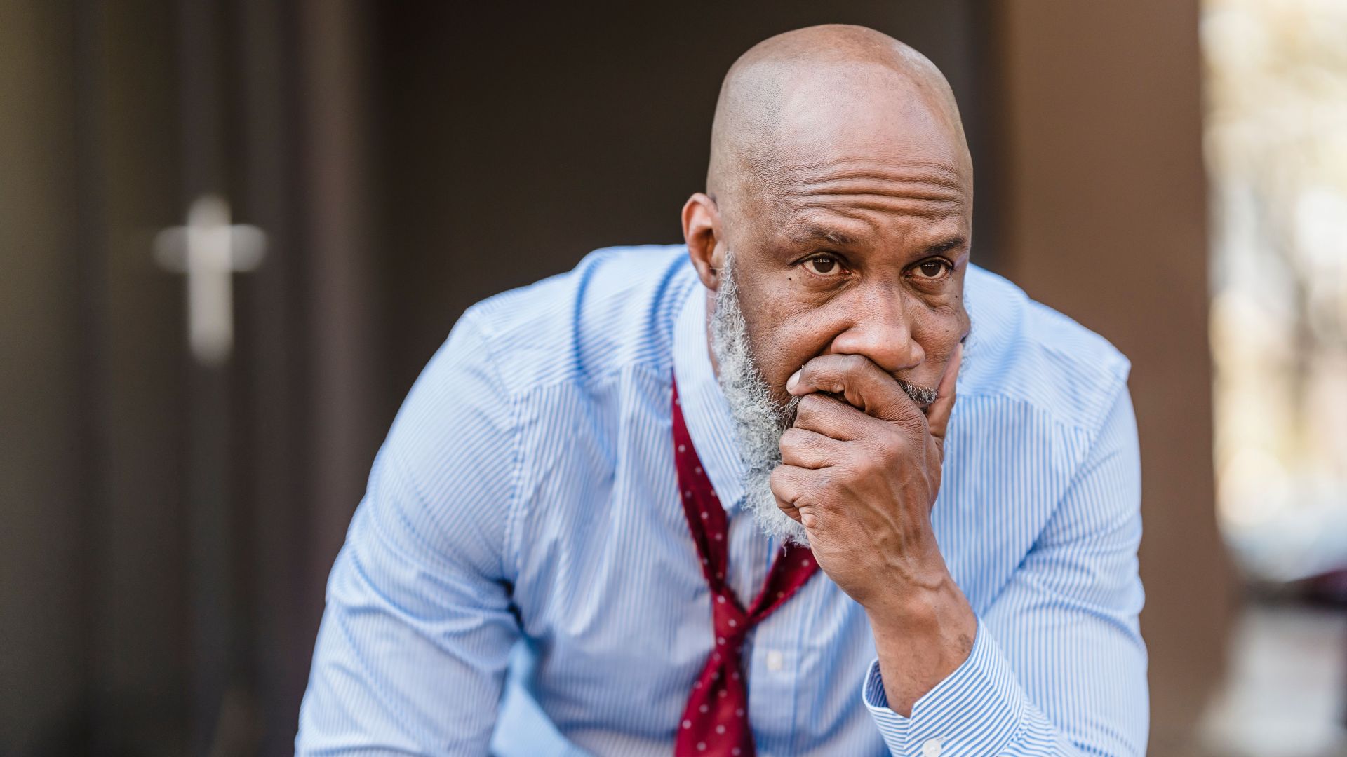 Unhappy bearded African American male worker in classy wear with hand on mouth looking away with concern while sitting on street