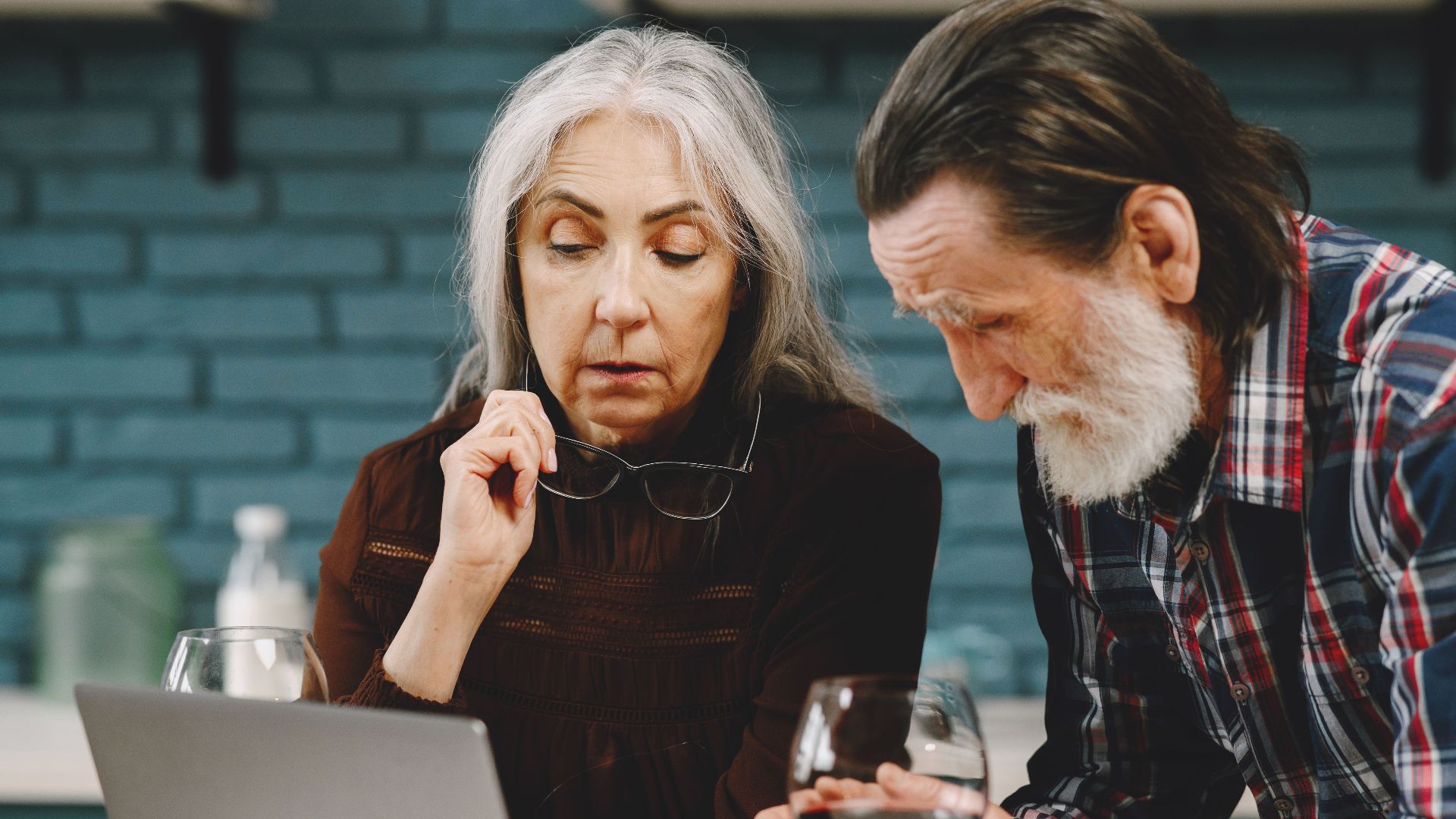 Elderly couple viewing a laptop together, enjoying a quiet moment with wine indoors.
