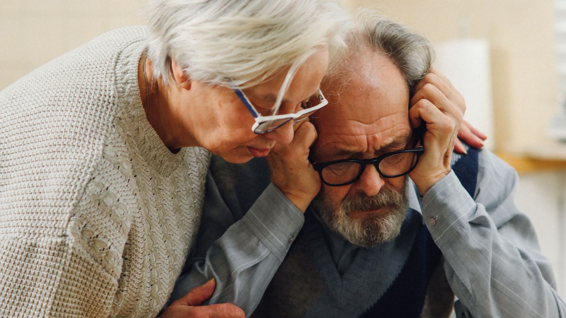 A worried senior couple reviews important documents at their kitchen table.