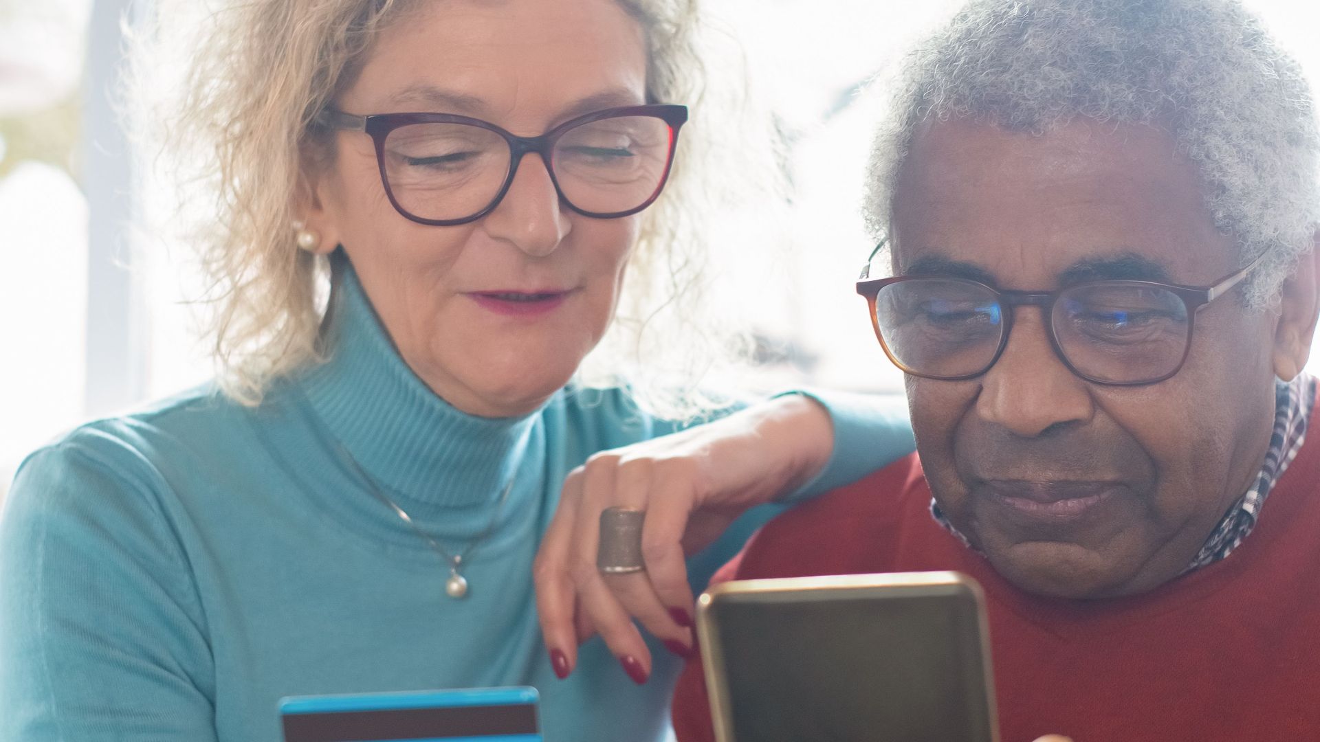 Elderly couple using smartphone and credit card for online shopping indoors.