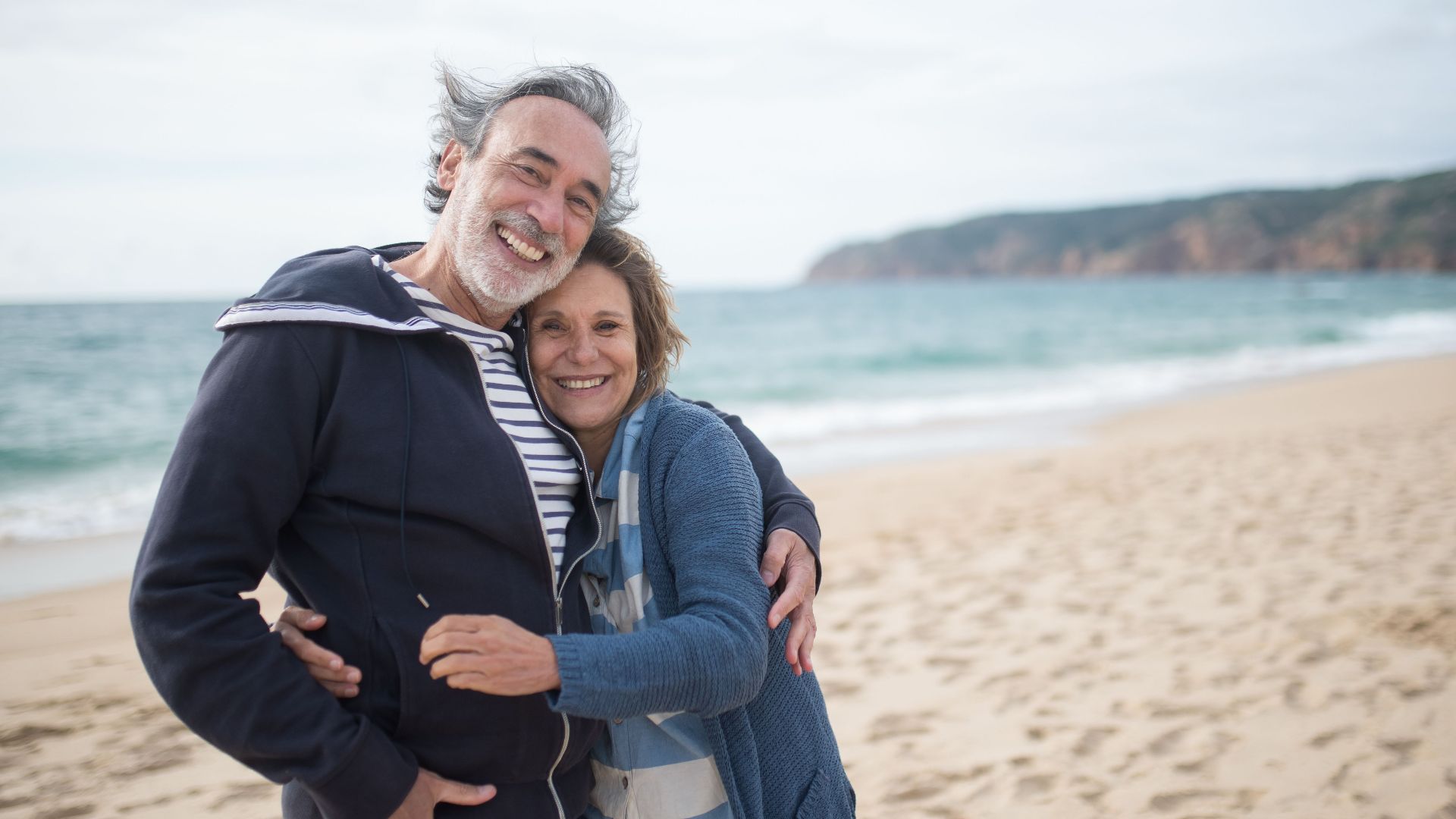 Happy senior couple embracing on a sandy beach in Portugal, symbolizing love and togetherness.