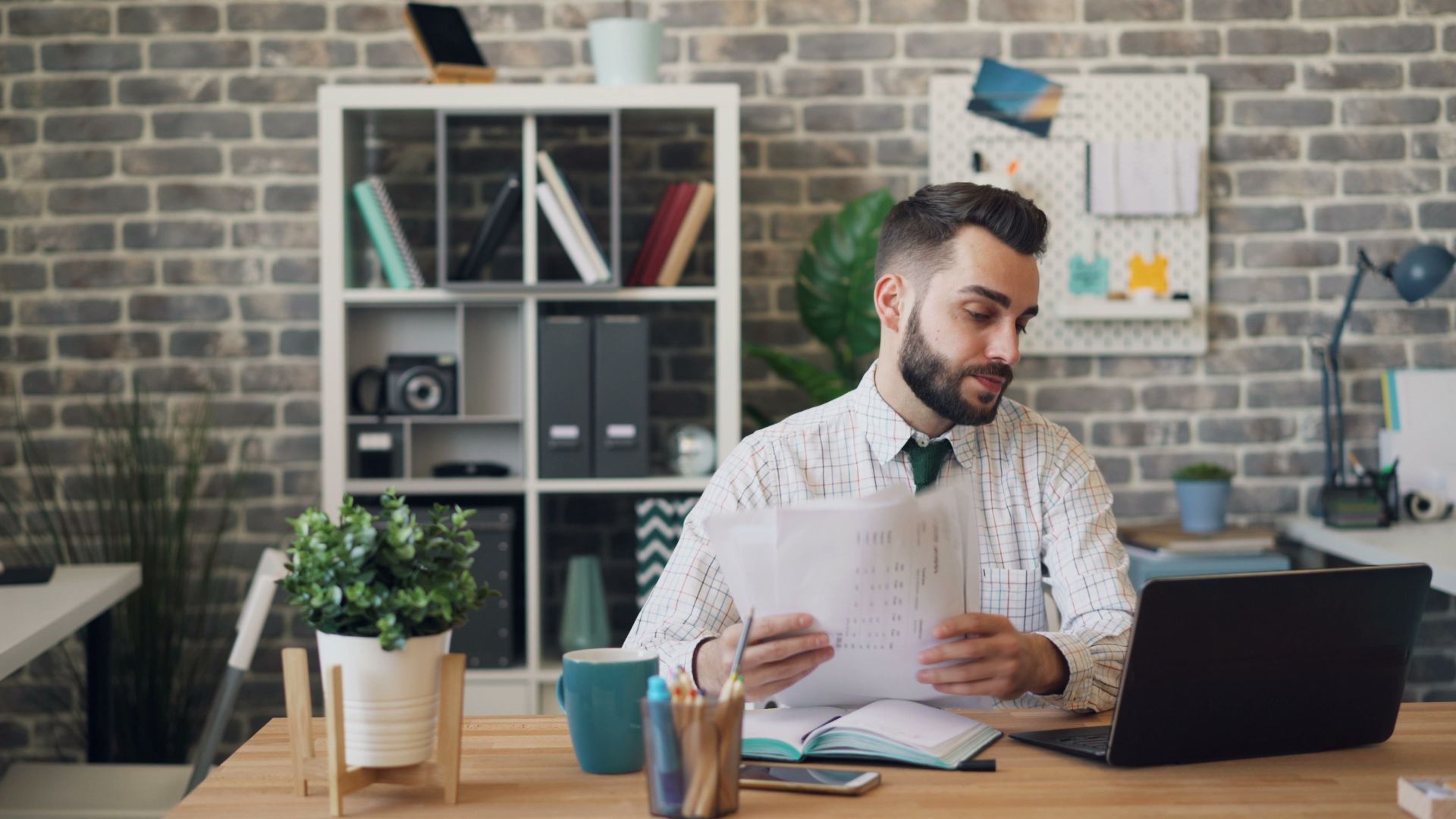 Young professional man at desk with laptop and documents in a modern office.