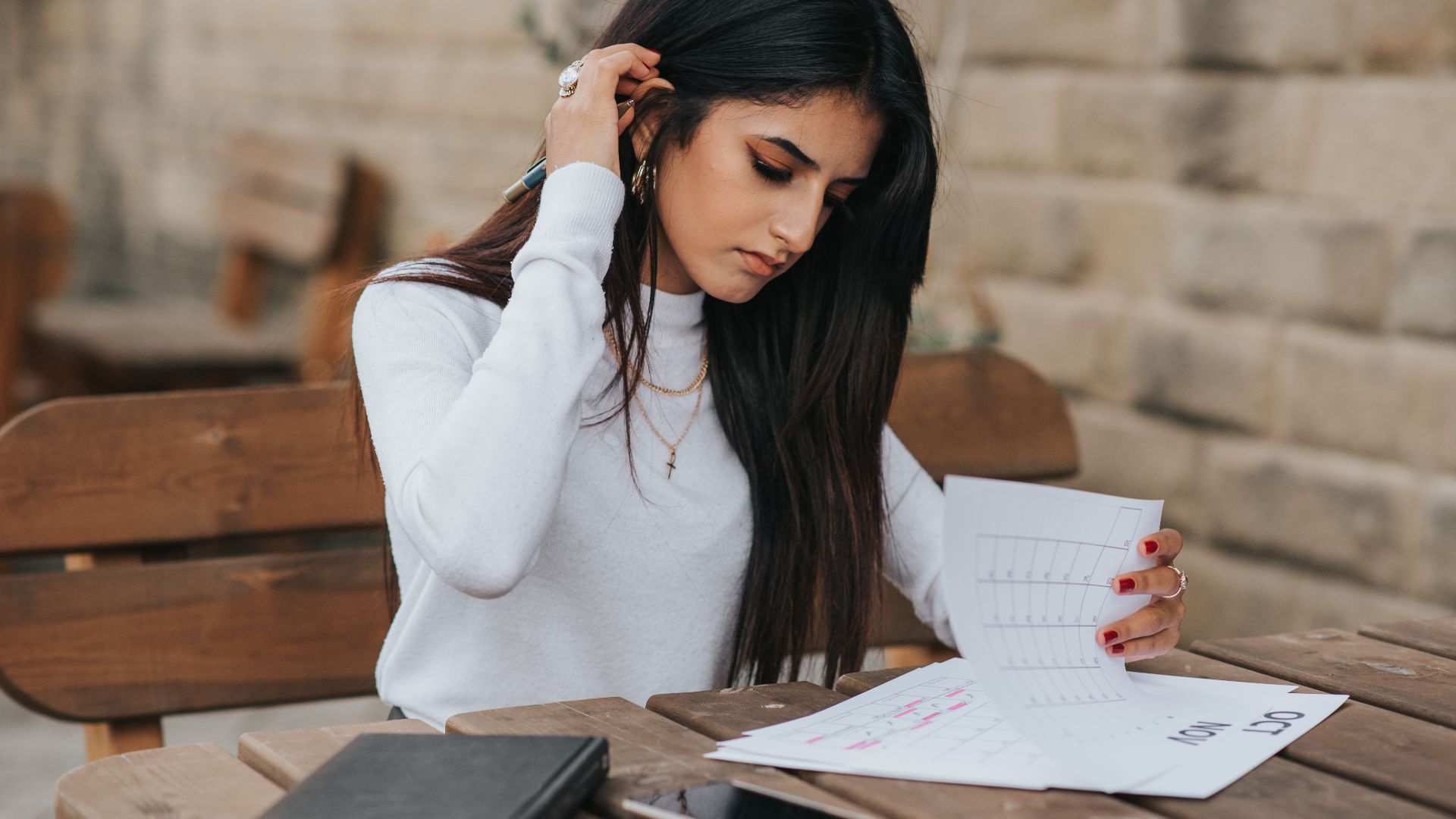 Young ethnic female student in casual outfit with dark hair at wooden table looking through plans in calendar