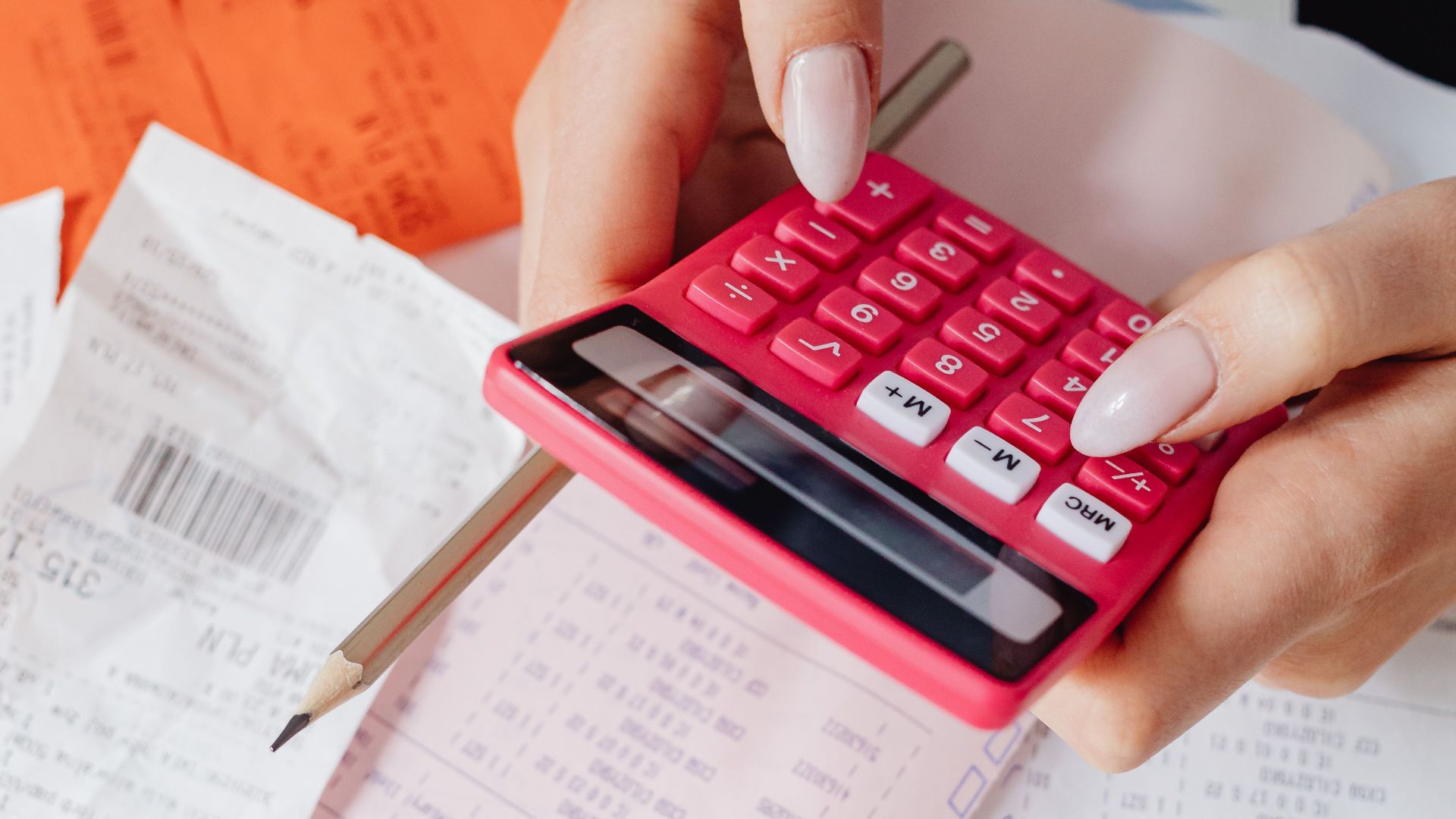 Hands using a red calculator surrounded by financial documents and receipts, symbolizing financial management.
