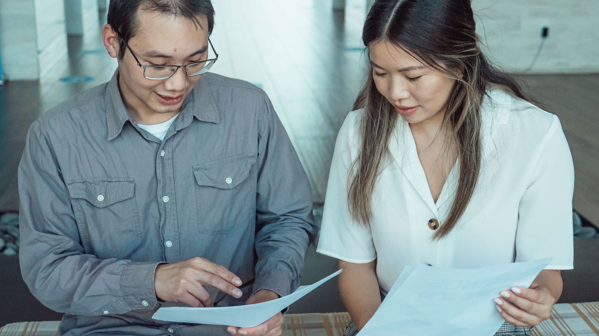 Two coworkers reviewing documents in a modern office, focused on teamwork and planning.