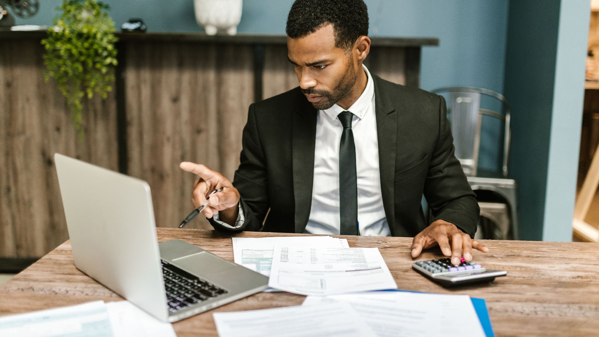Professional man in a suit using a laptop and calculator in an office setting.