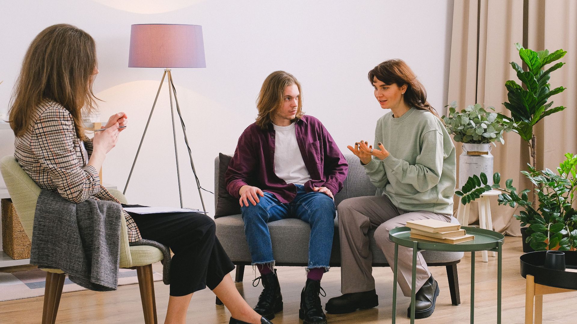 Young couple sitting on sofa and talking with woman psychologist in light room in daytime