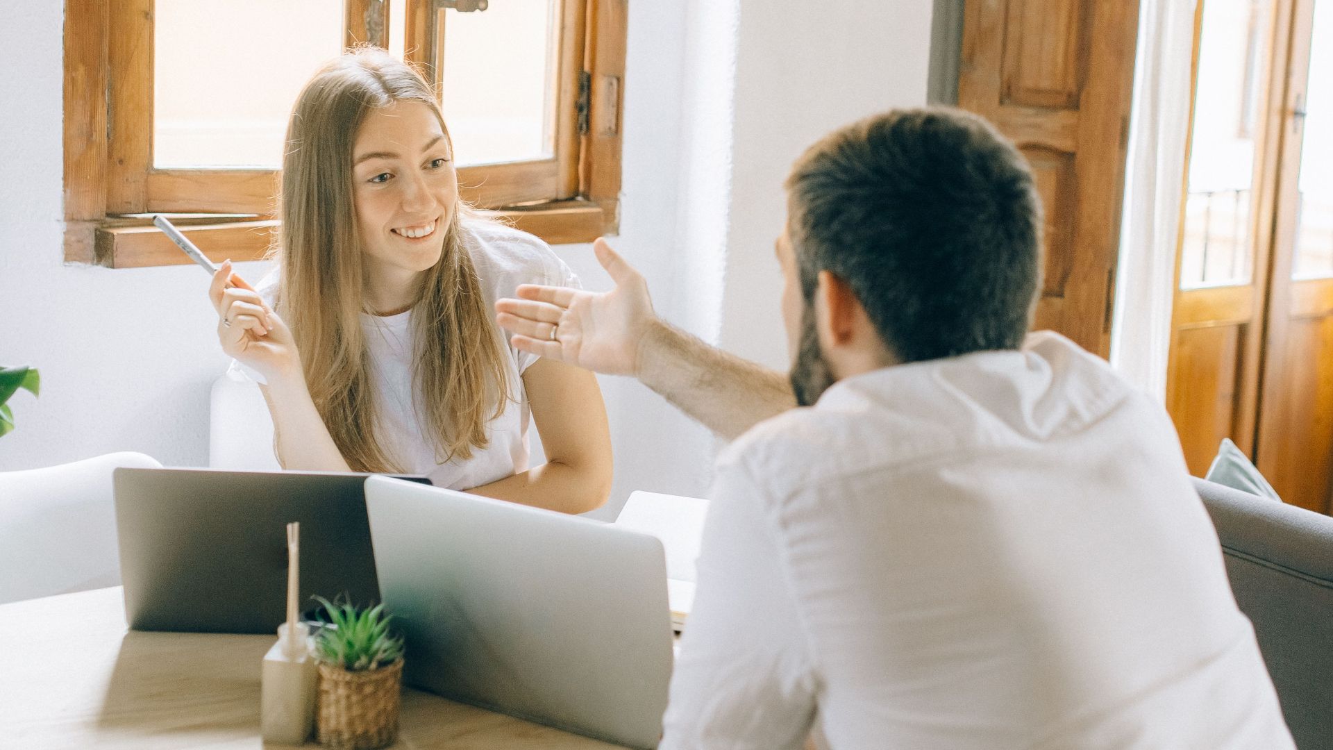 A man and woman discussing ideas while working remotely with laptops in a cozy home setting.