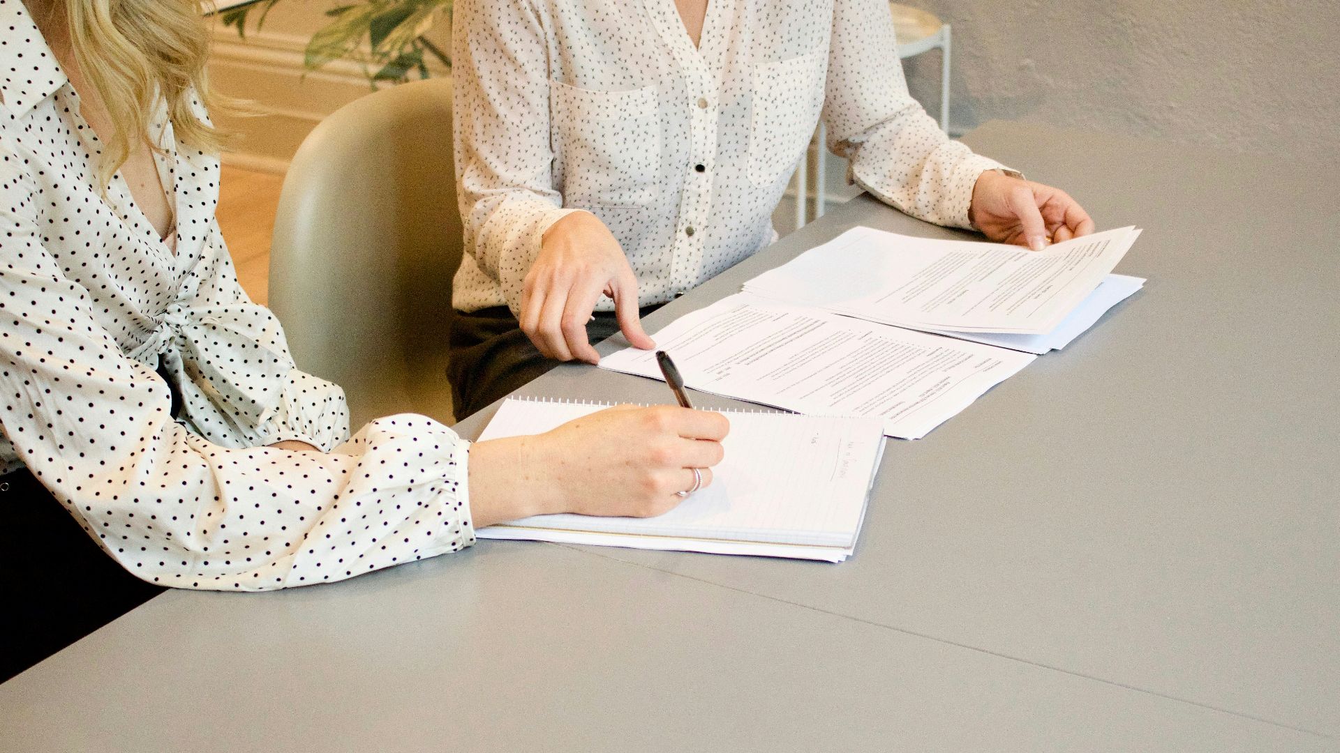 woman signing on white printer paper beside woman about to touch the documents