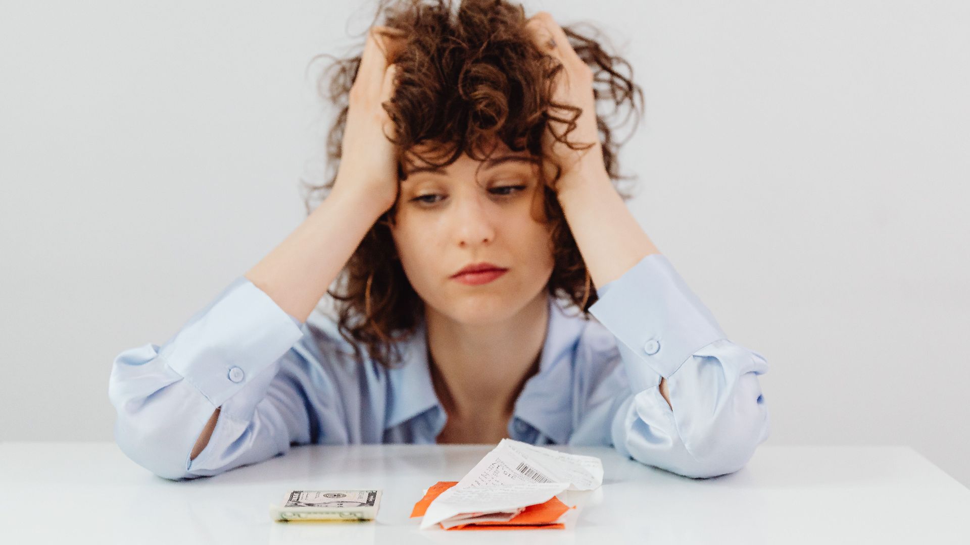 Woman in blue sleeves appears stressed while looking at receipts and money, symbolizing financial stress.