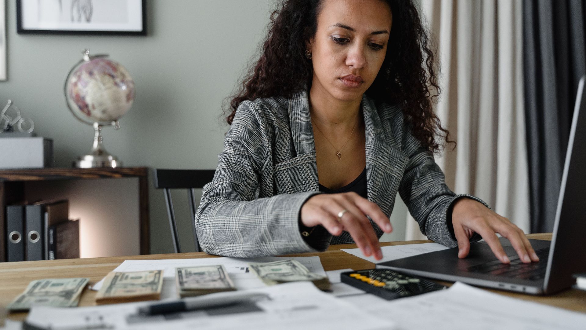 Professional woman analyzing financial documents and counting cash at office desk.