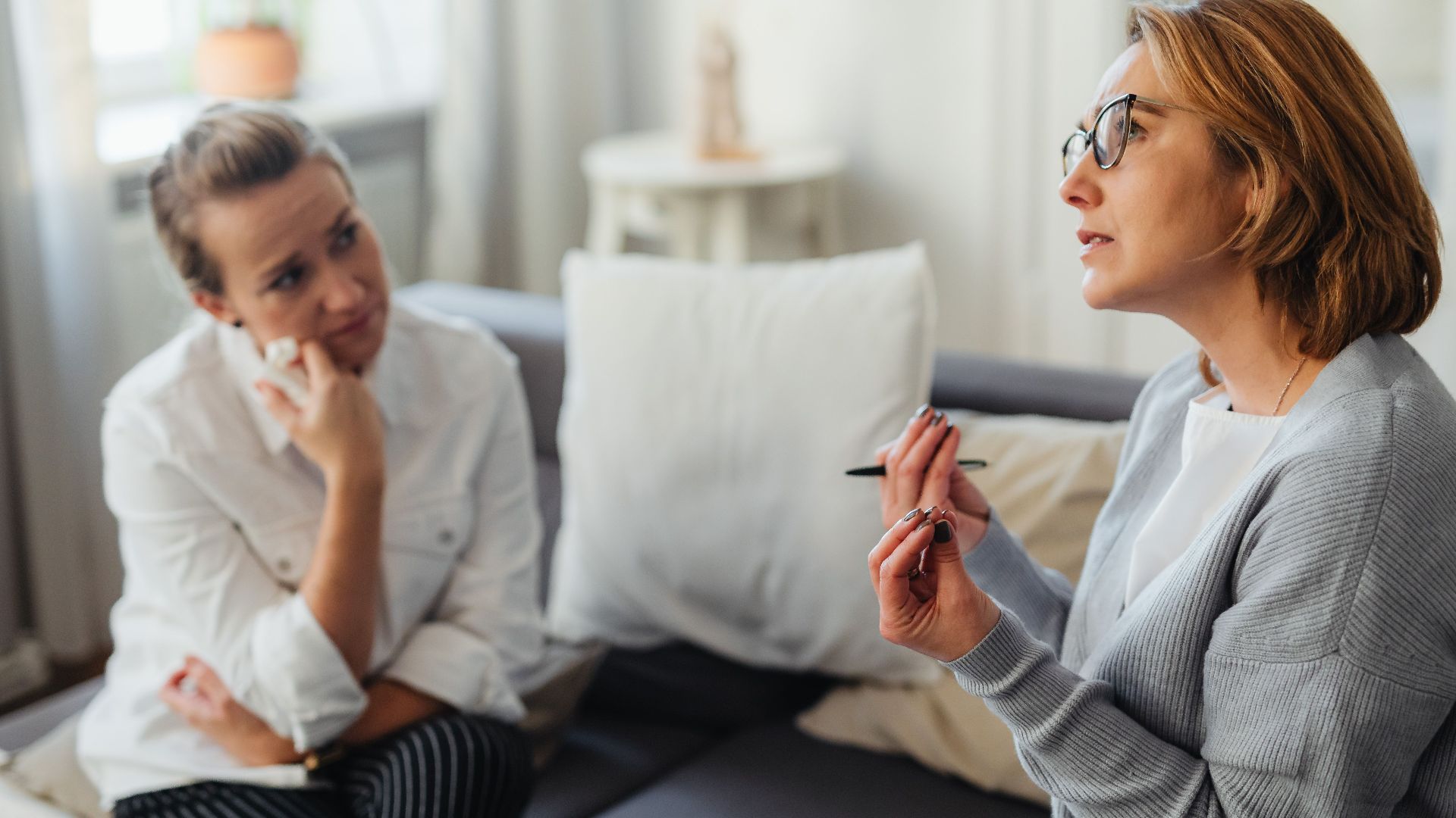 Two women engaged in a thoughtful counseling session in a cozy indoor setting.