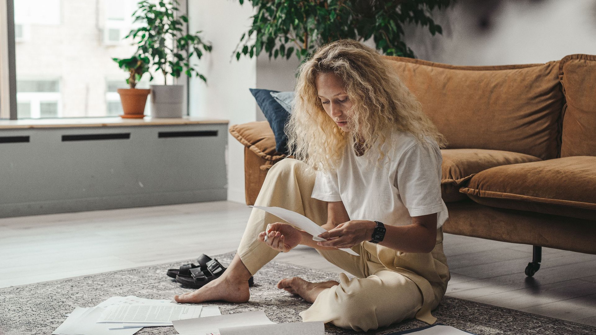 Woman sitting on the floor at home, reviewing paperwork in a relaxed environment.